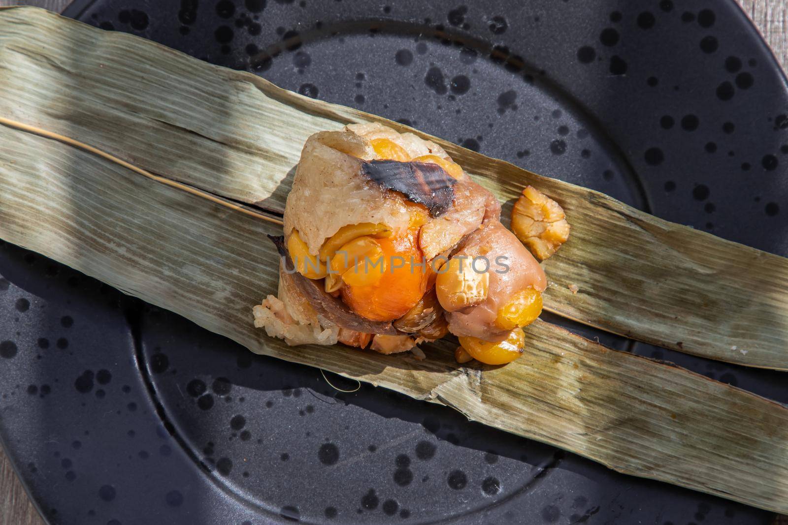 Chinese rice dumpling (Zongzi) shaped pyramidal wrapped by leaves ingredients on dried banana leaf. Famous asian tasty handmade food in dragon boat (duan wu) festival occasion.