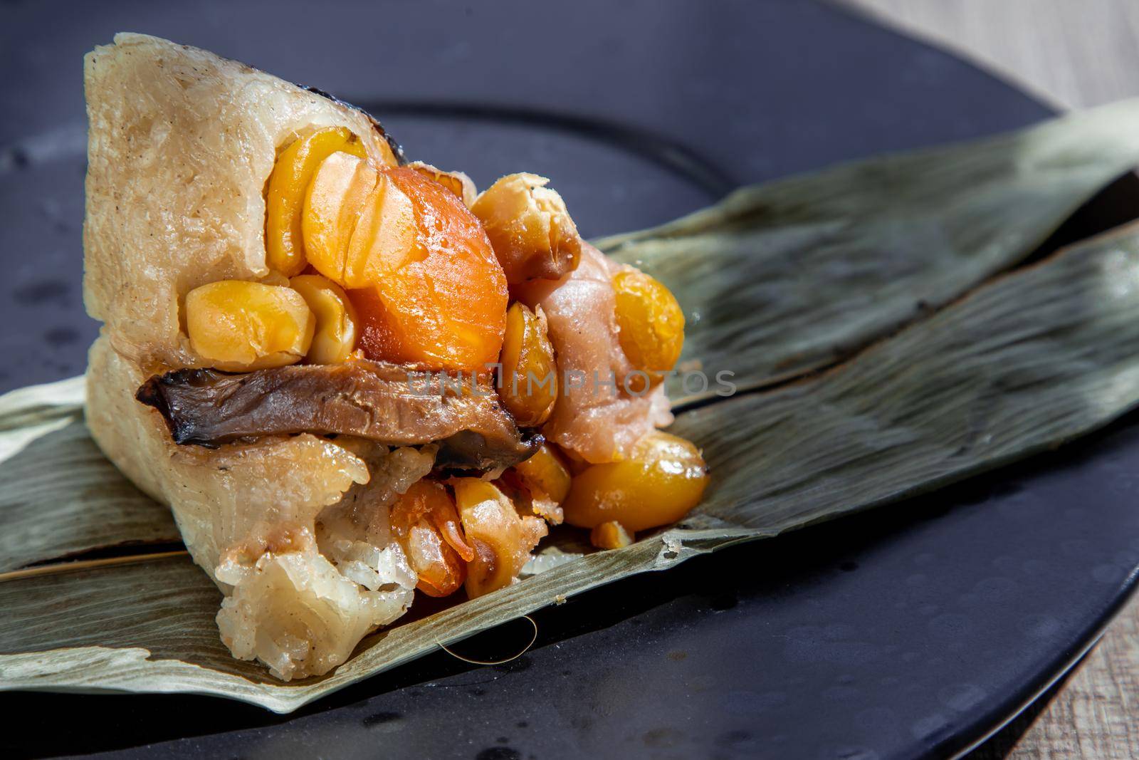 Chinese rice dumpling (Zongzi) shaped pyramidal wrapped by leaves ingredients on dried banana leaf. Famous asian tasty handmade food in dragon boat (duan wu) festival occasion.
