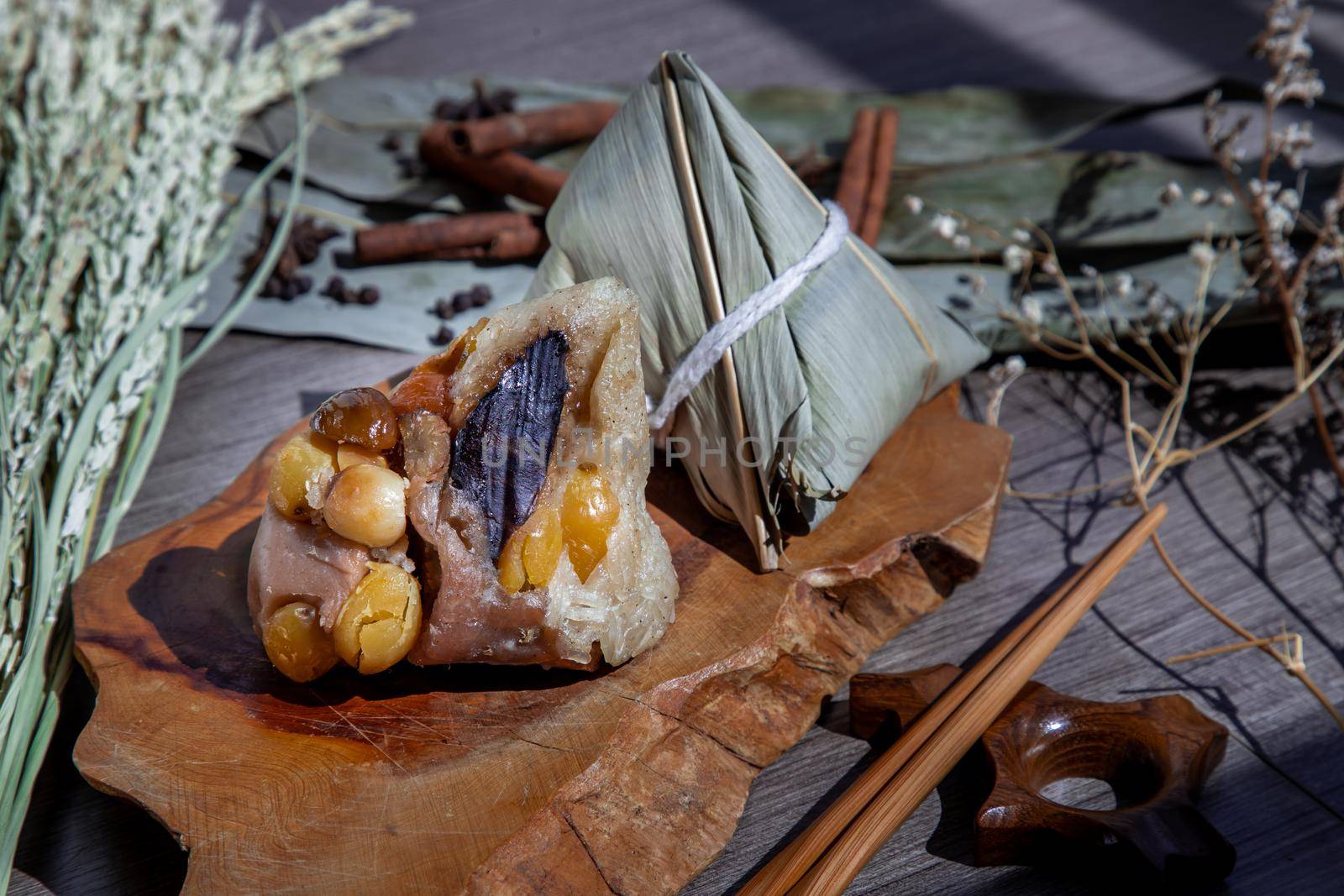 Chinese rice dumpling (Zongzi) shaped pyramidal wrapped by leaves ingredients on wooden plate and chopsticks. Famous asian tasty handmade food in dragon boat (duan wu) festival occasion.