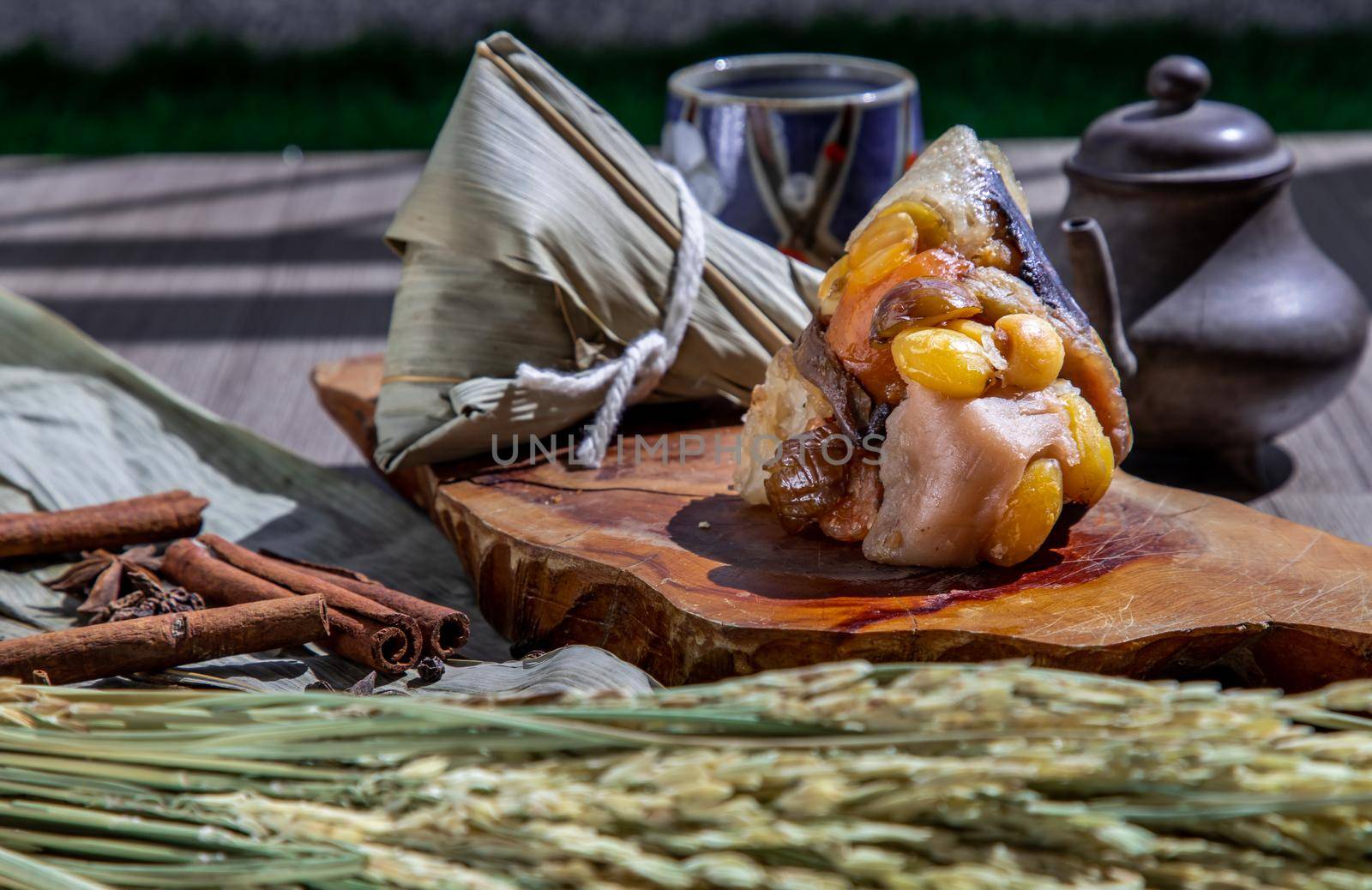 Chinese rice dumpling (Zongzi) shaped pyramidal wrapped by leaves ingredients on wooden plate Served with chinese tea. Famous asian tasty handmade food in dragon boat (duan wu) festival occasion.