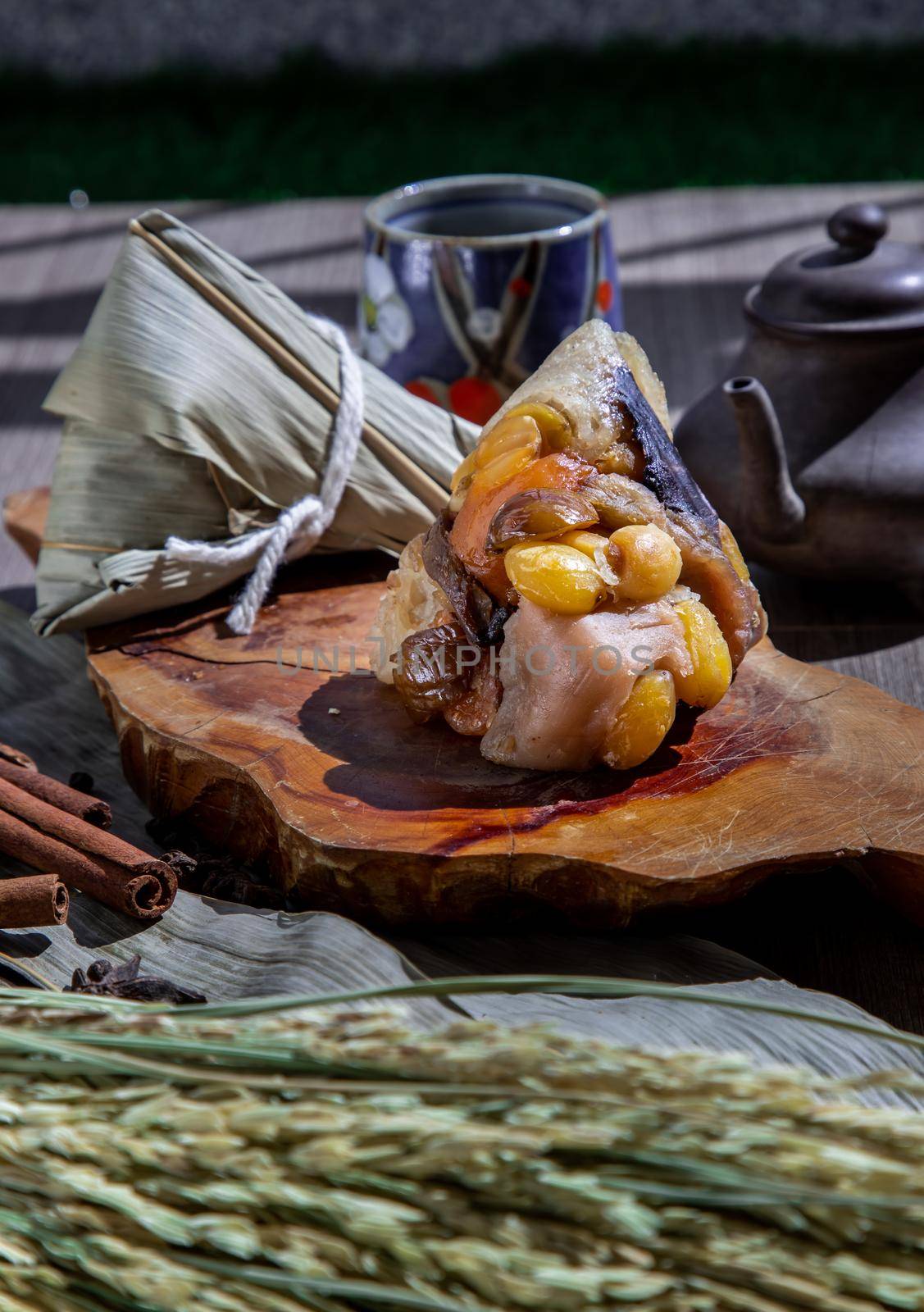 Chinese rice dumpling (Zongzi) shaped pyramidal wrapped by leaves ingredients on wooden plate Served with chinese tea. Famous asian tasty handmade food in dragon boat (duan wu) festival occasion.