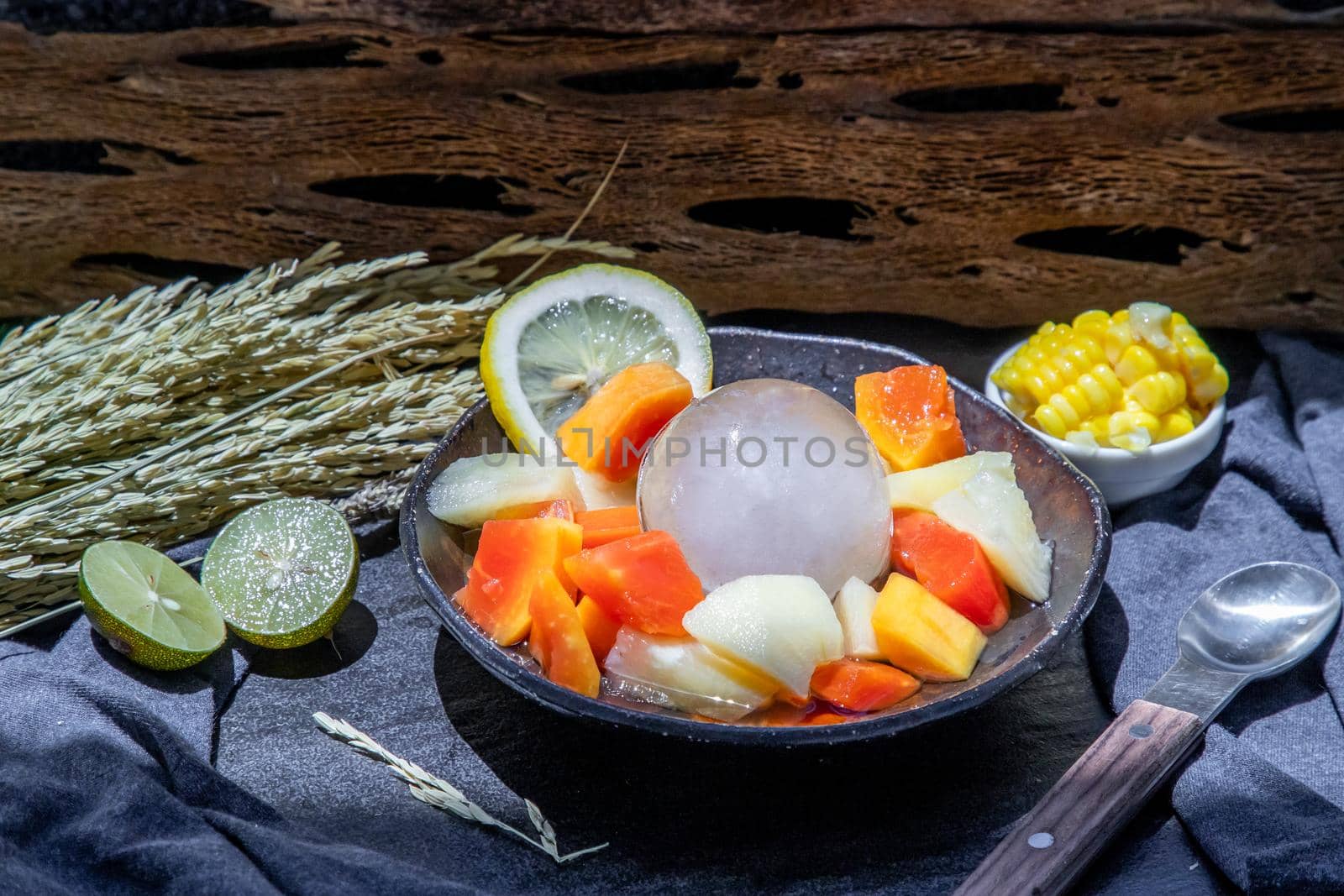 Tropical fresh fruit salad served with corn on black ceramic bowl in dark background.  Selective focus.