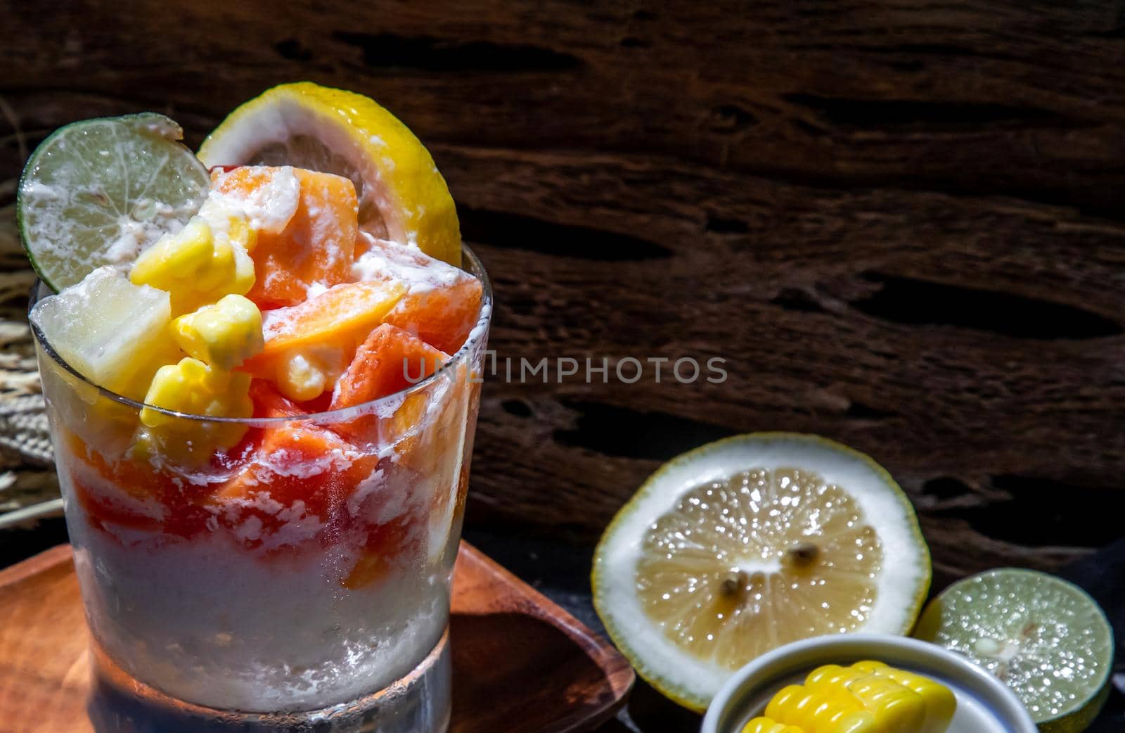 Tropical fresh fruit salad with milk and oatmeal in a glass cup served with corn on dark background. Sweet healthy breakfast, Healthy vegan meal. Selective focus.
