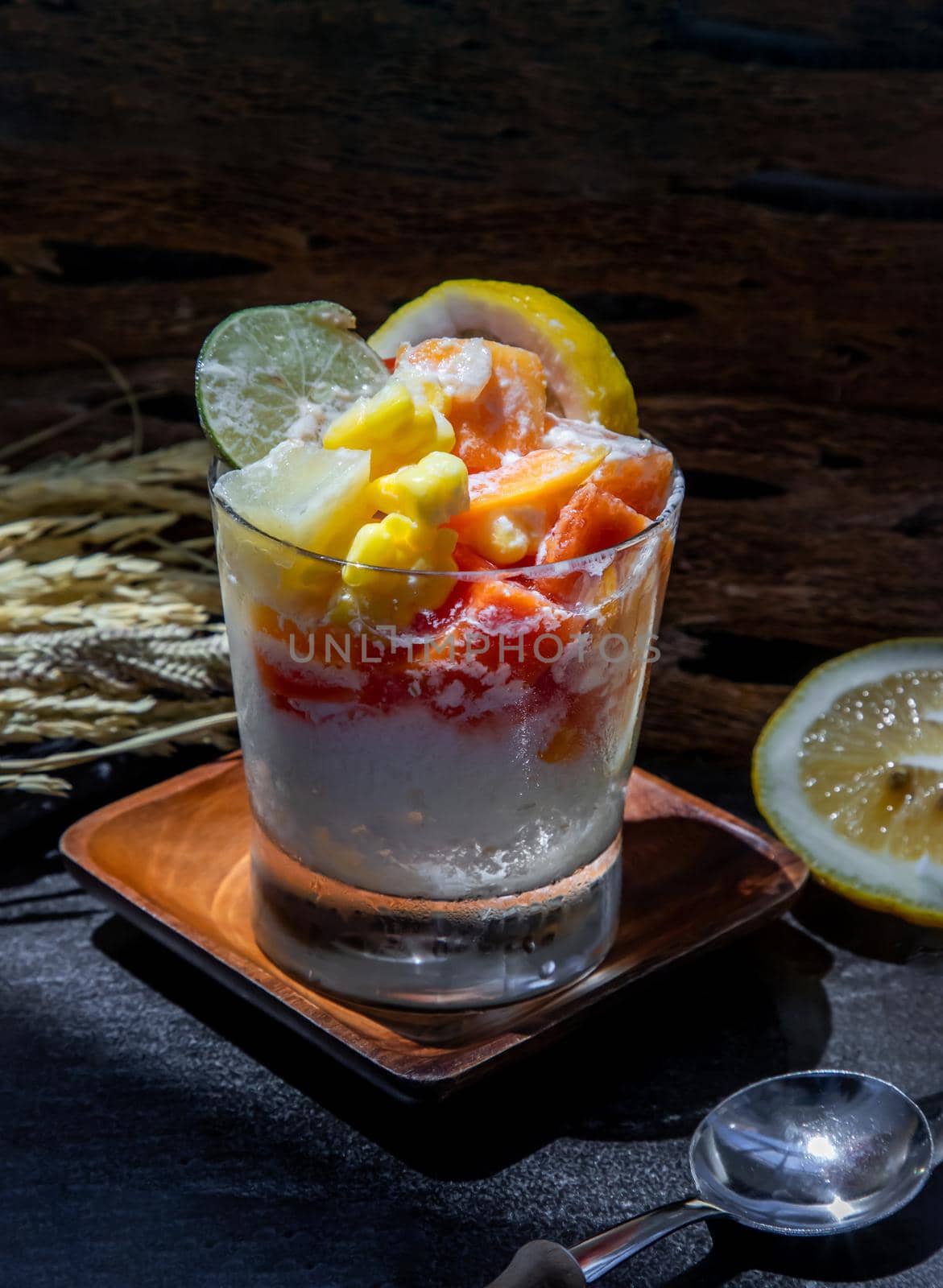 Tropical fresh fruit salad with milk and oatmeal in a glass cup on dark background. Sweet healthy breakfast, Healthy vegan meal. Selective focus.