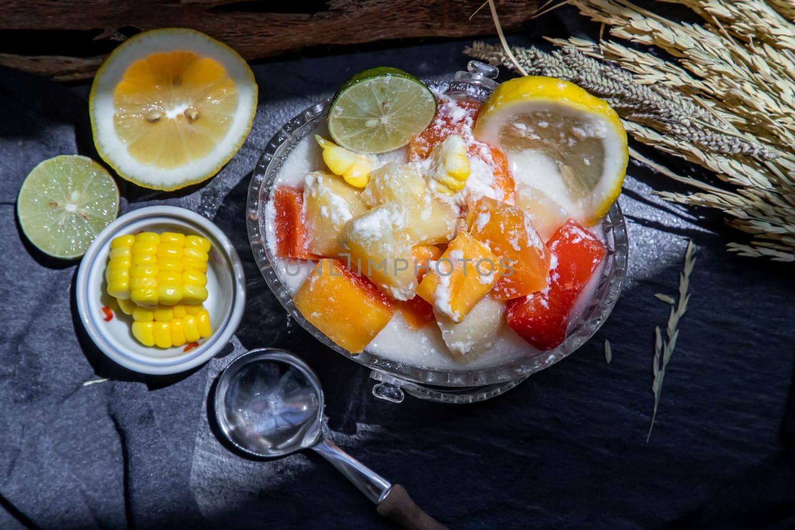 Tropical fresh fruit salad with milk and oatmeal  in a glass bowl served with corn on dark background. Sweet healthy breakfast, Healthy vegan meal. Top view, Selective focus.