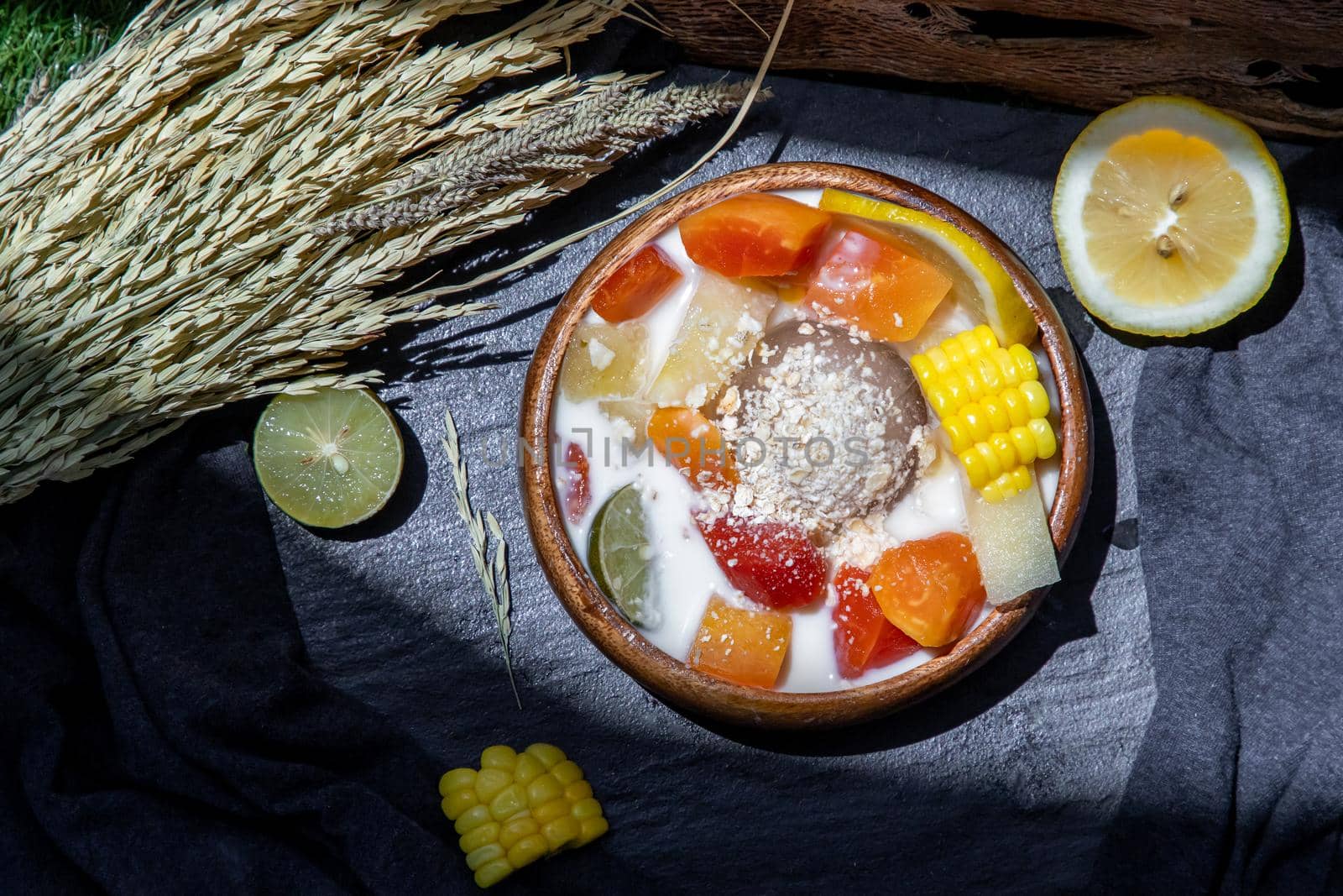 Tropical fresh fruit salad with milk and oatmeal on wooden bowl in dark background. Sweet healthy breakfast, Healthy vegan meal, Selective focus.