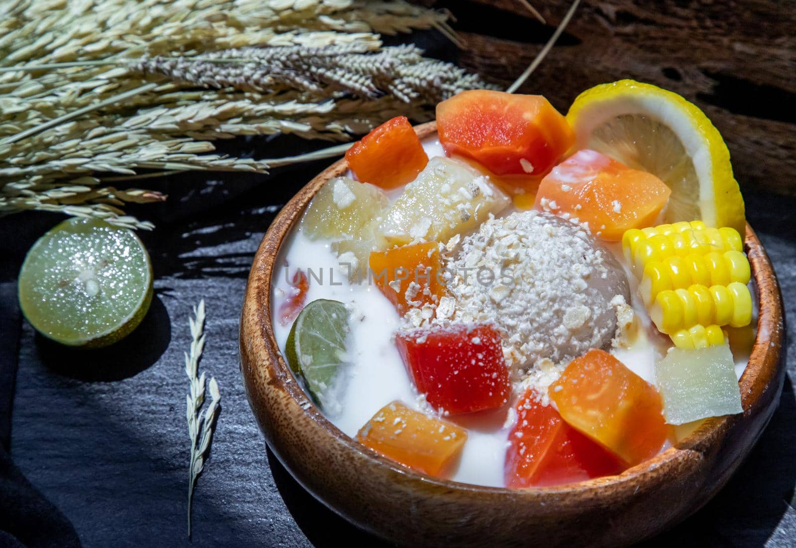 Tropical fresh fruit salad with milk and oatmeal on wooden bowl in dark background. Sweet healthy breakfast, Healthy vegan meal, Selective focus.