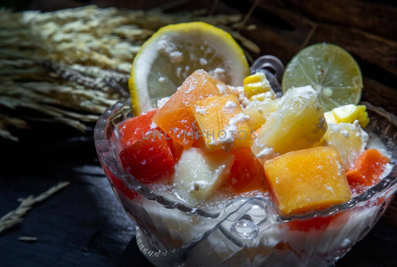 Tropical fresh fruit salad with milk and oatmeal in a glass bowl on dark background. Sweet healthy breakfast, Healthy vegan meal. Selective focus.