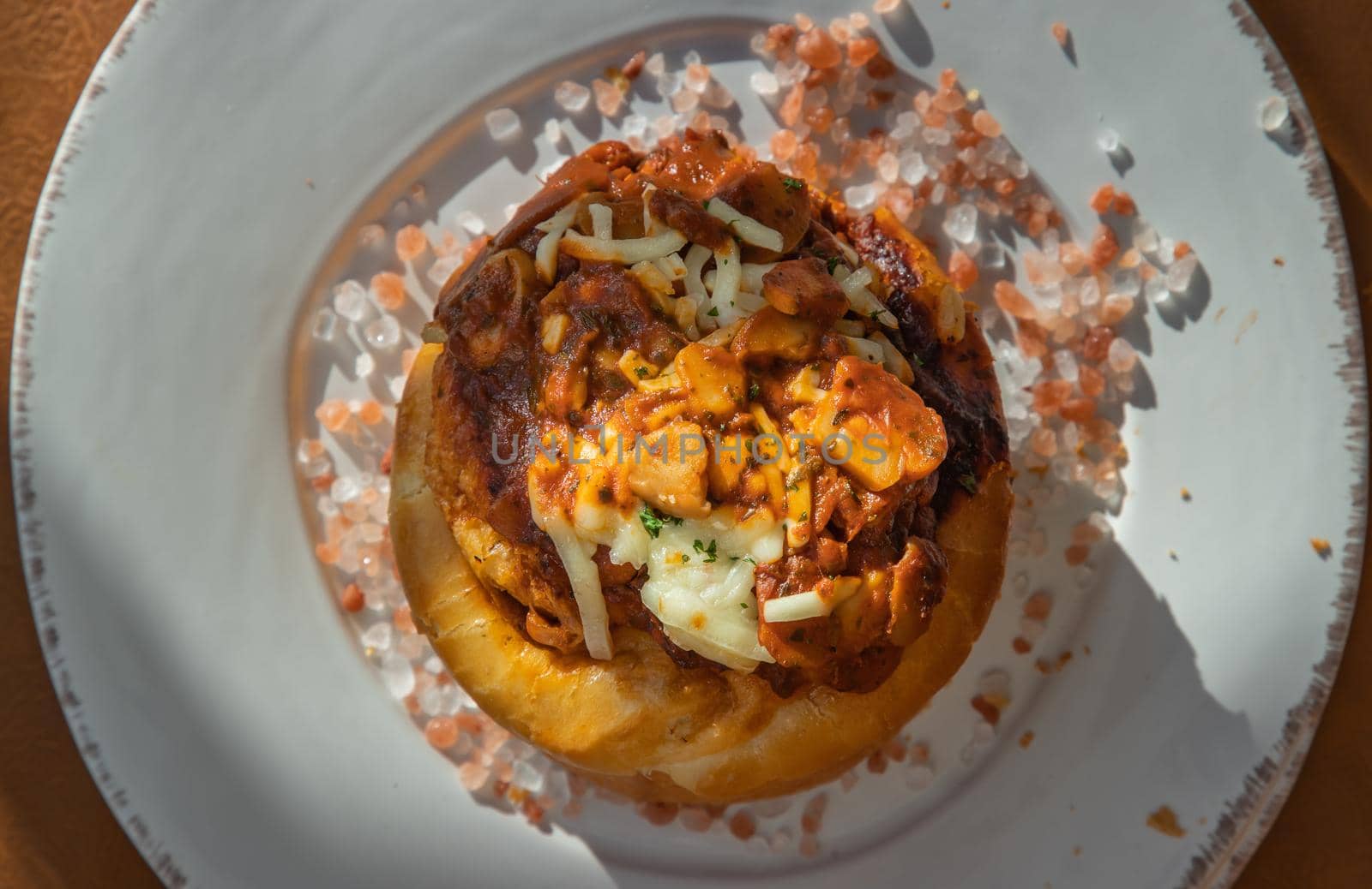 Homemade pizza buns topped with tomato sauce, ham, sausage, green onion and mozzarella cheese with himalayan pink salt on classic white plate.