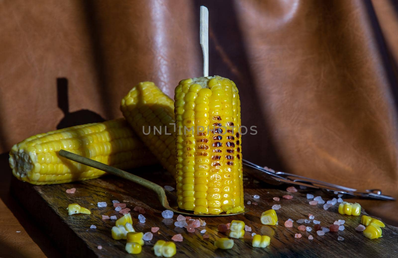 Grilled corn on the cob  on rustic wooden board over brown leather background.  by tosirikul