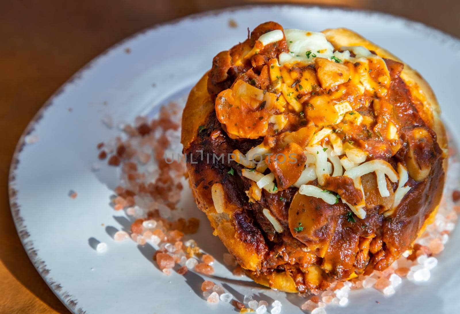 Homemade pizza buns topped with tomato sauce, ham, sausage, green onion and mozzarella cheese with himalayan pink salt on classic white plate.