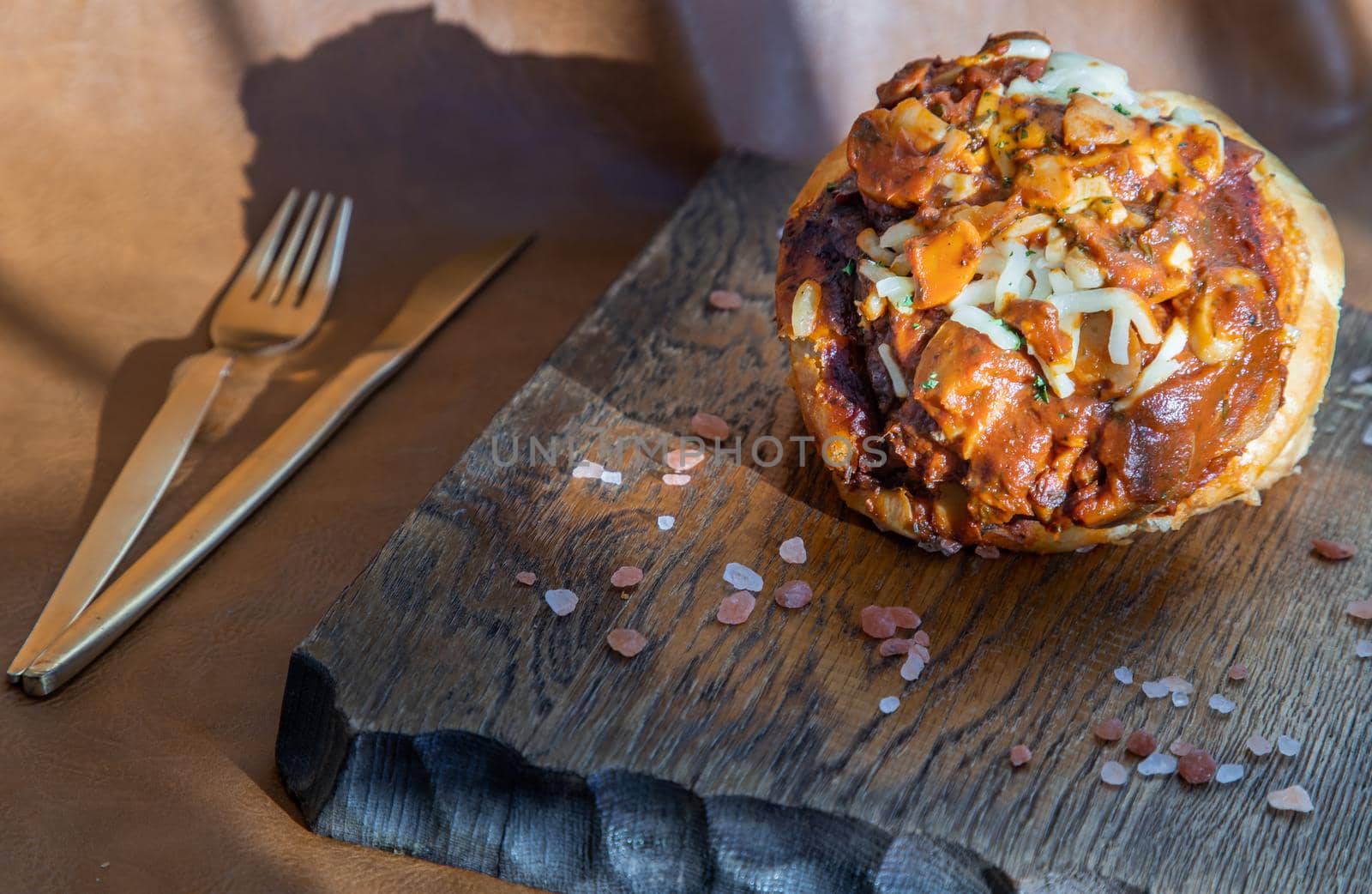 Homemade pizza buns topped with tomato sauce, ham, sausage, green onion and mozzarella cheese with himalayan pink salt on rustic wooden board.