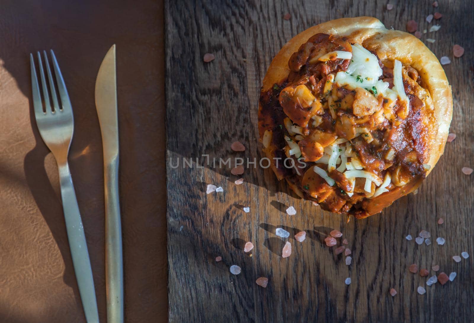 Homemade pizza buns topped with tomato sauce, ham, sausage, green onion and mozzarella cheese with himalayan pink salt on rustic wooden board.