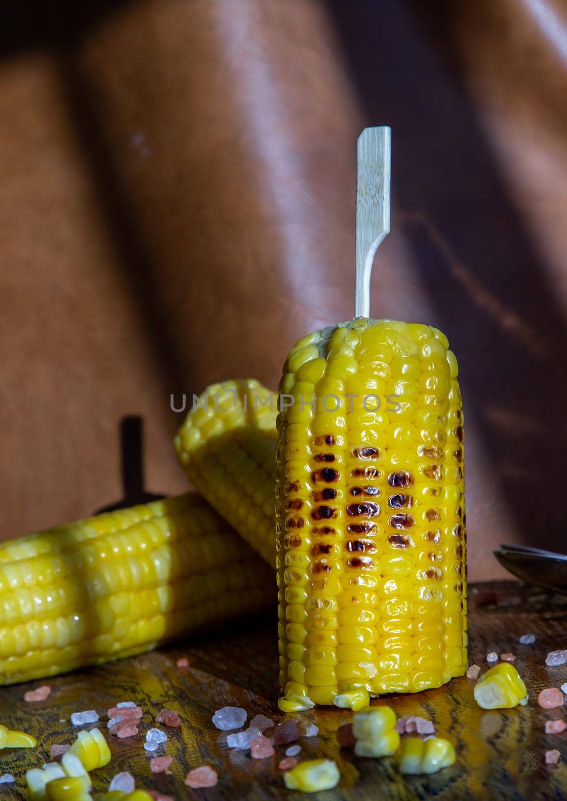 Grilled corn on the cob  on rustic wooden board over brown leather background.  by tosirikul