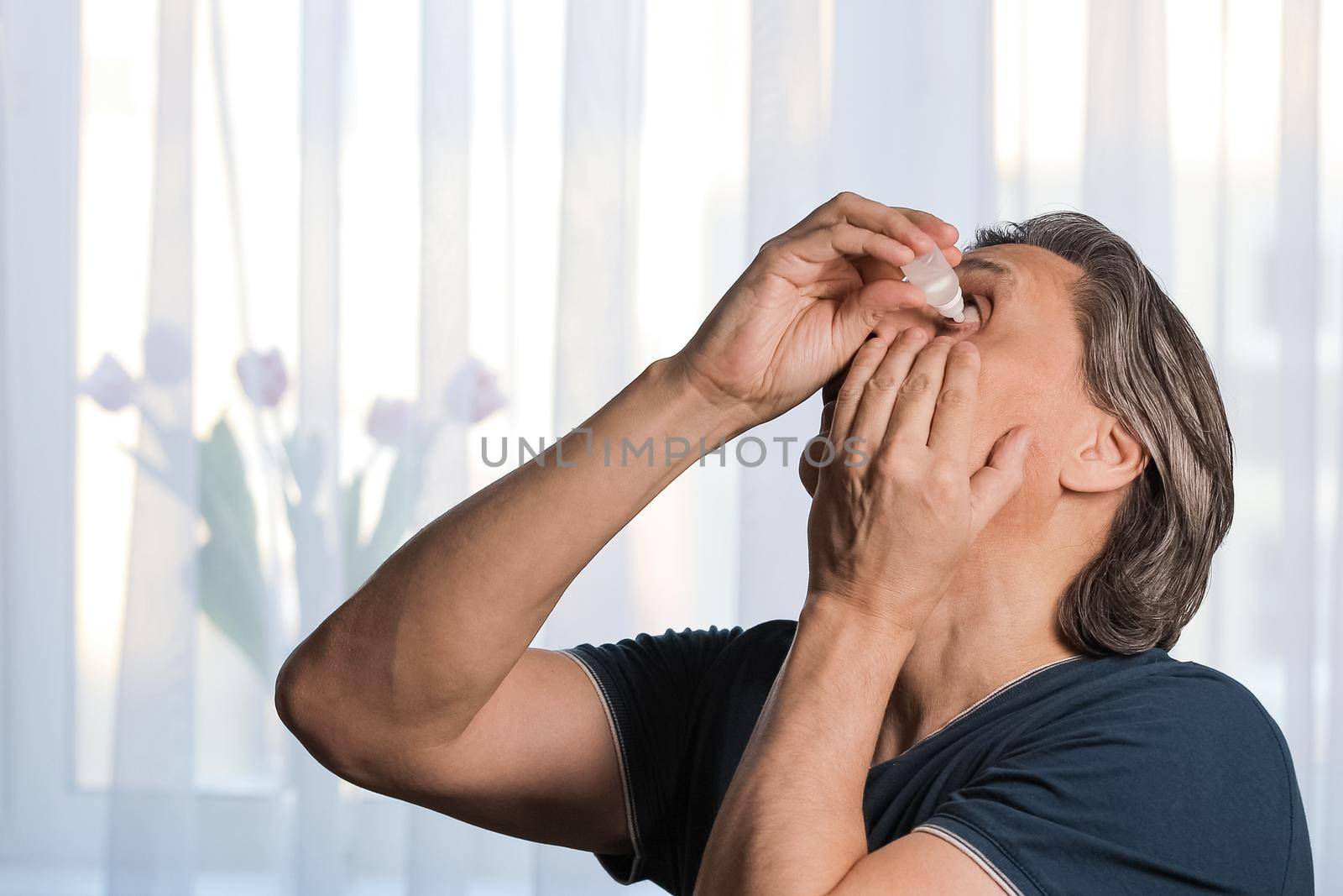 An adult gray-haired man is dripping eye drops. Dry eyes. Close-up