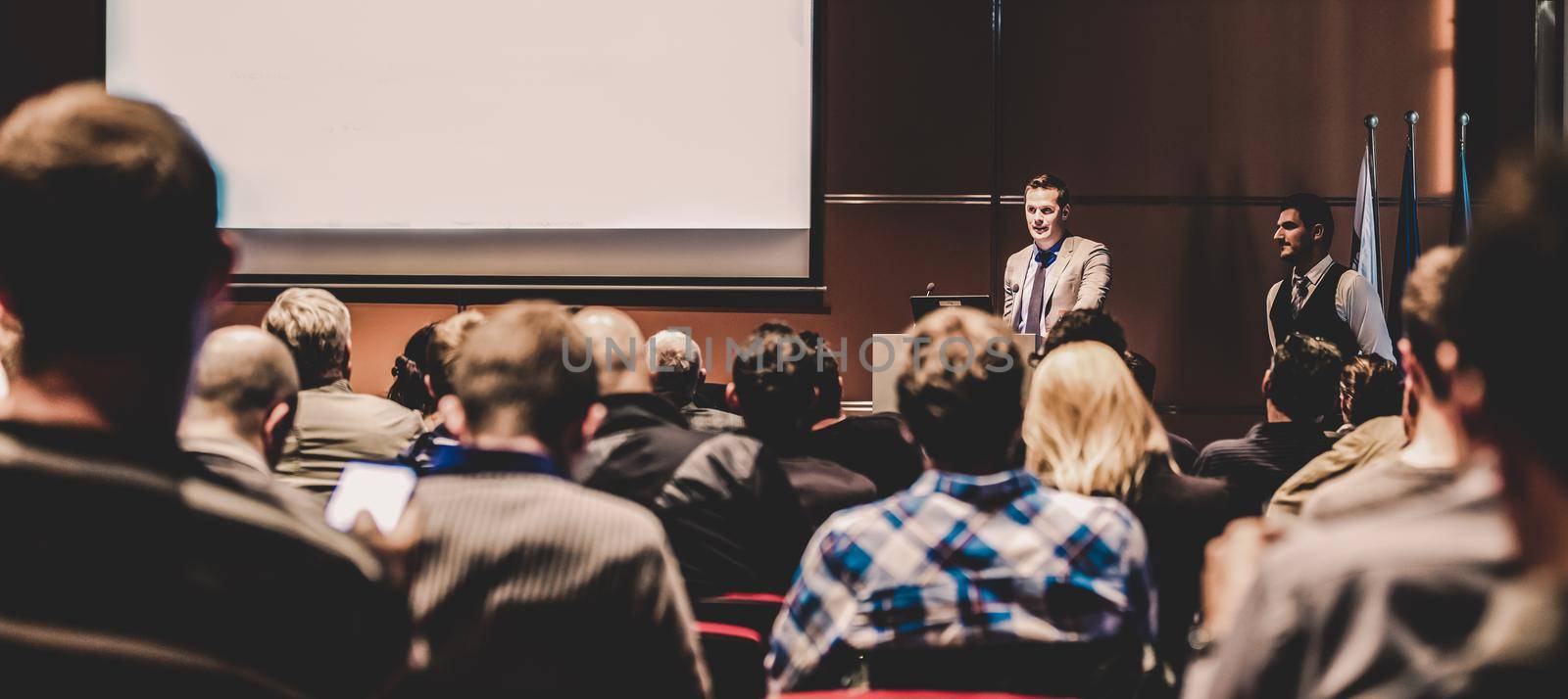 Speaker giving a talk in conference hall at business meeting event. Rear view of unrecognizable people in audience at the conference hall. Business and entrepreneurship concept.