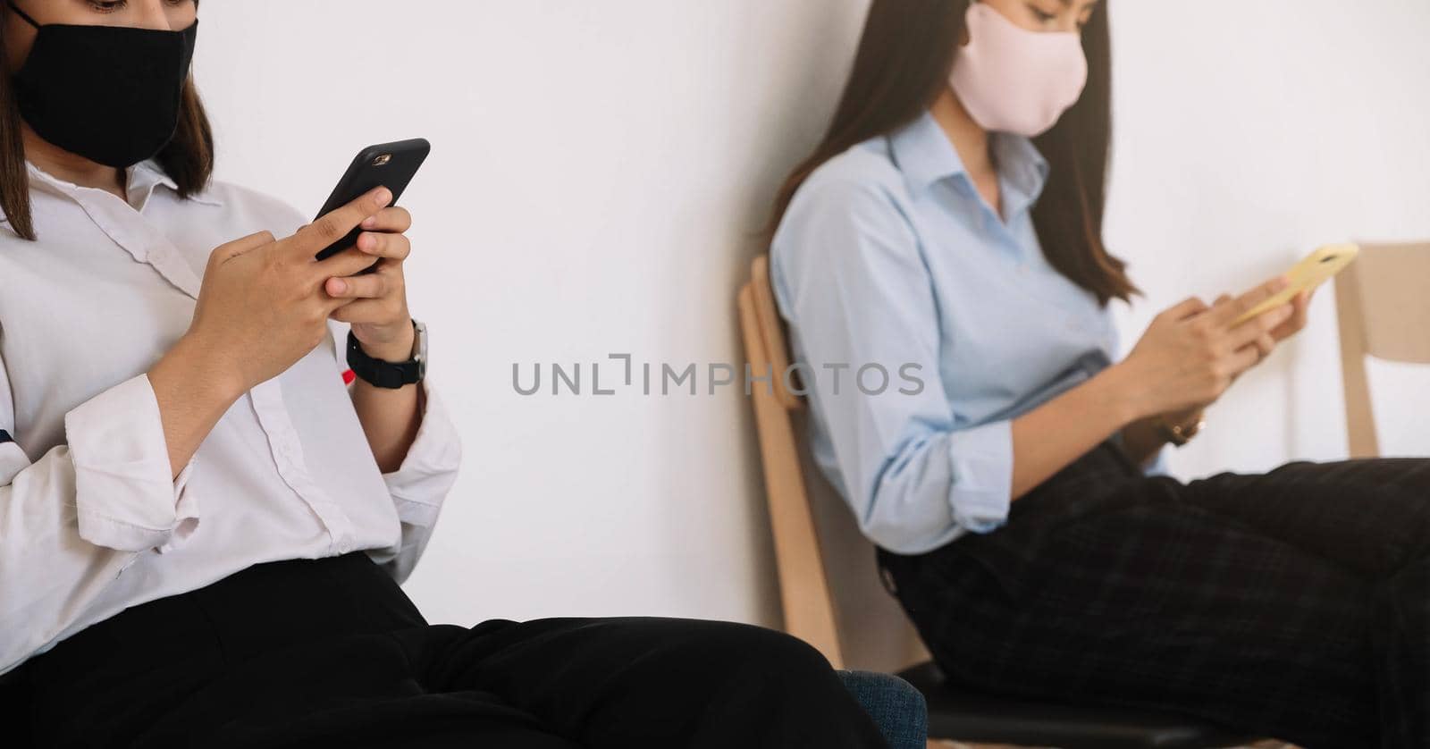 Two Asian young woman chatting in smartphone and wearing mask sitting distance protect from COVID-19 viruses for social distancing for infection risk