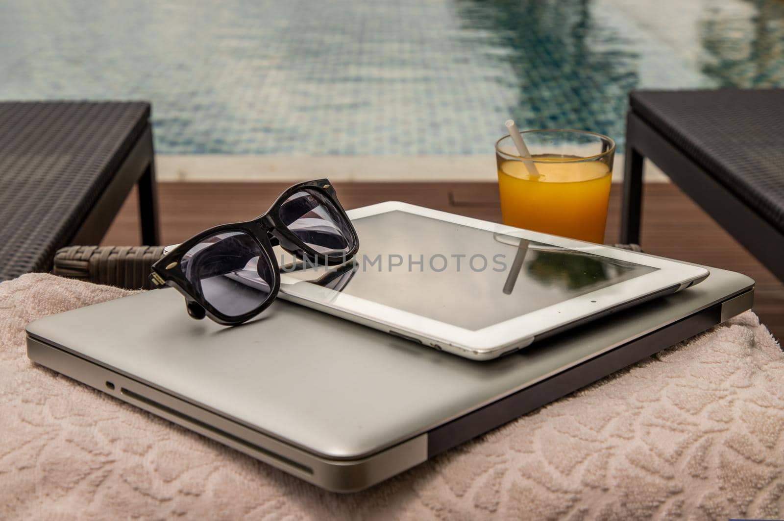 Relaxing moment by the pool. Take a break from working on laptop and tablet and enjoy the fresh orange juice for a refreshment.  Outdoor swimming pool background. leisure activity.