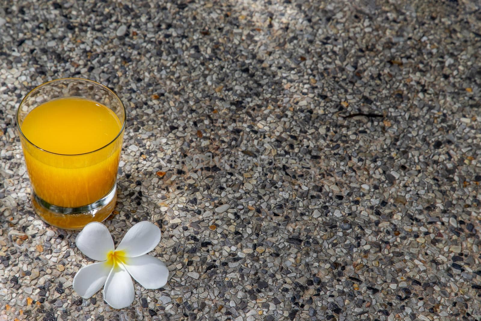 A glass of fresh orange juice with flower for a refreshment on stone background. leisure activity.