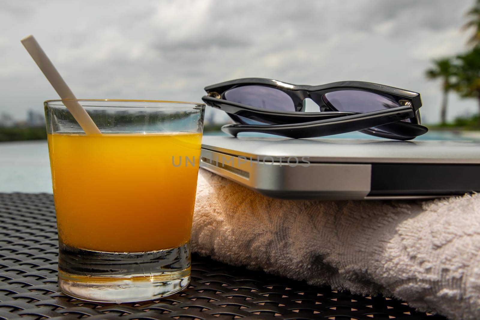 Relaxing moment by the pool. Take a break from working on laptop and enjoy the fresh orange juice for a refreshment.  Outdoor swimming pool background. leisure activity.