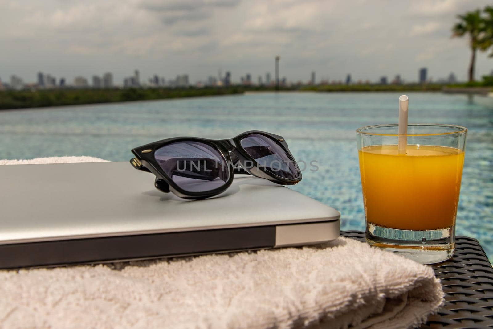 Relaxing moment by the pool. Take a break from working on laptop and enjoy the fresh orange juice for a refreshment.  Outdoor swimming pool background. leisure activity.