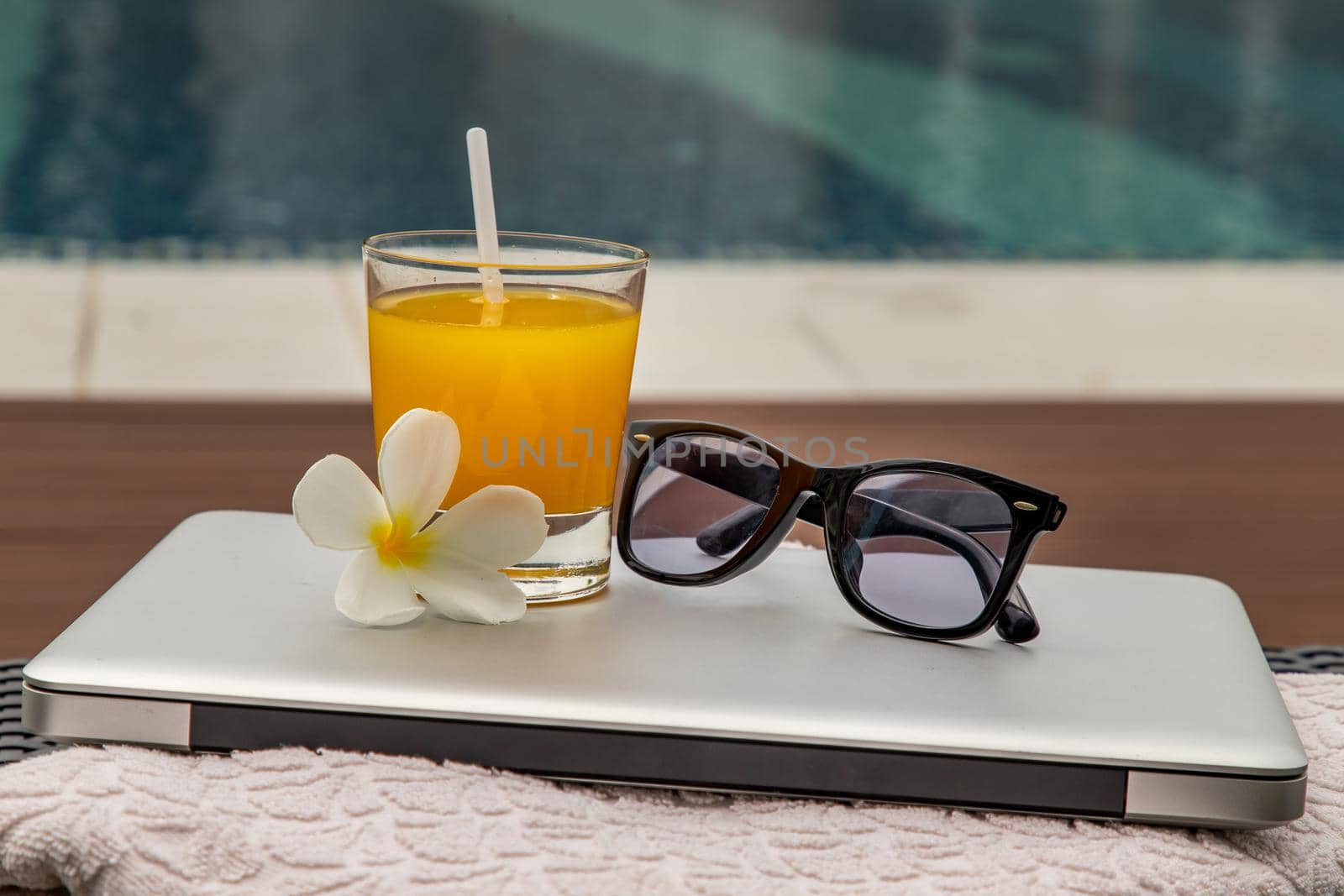Relaxing moment by the pool. Take a break from working on laptop and enjoy the fresh orange juice for a refreshment.  Outdoor swimming pool background. leisure activity.