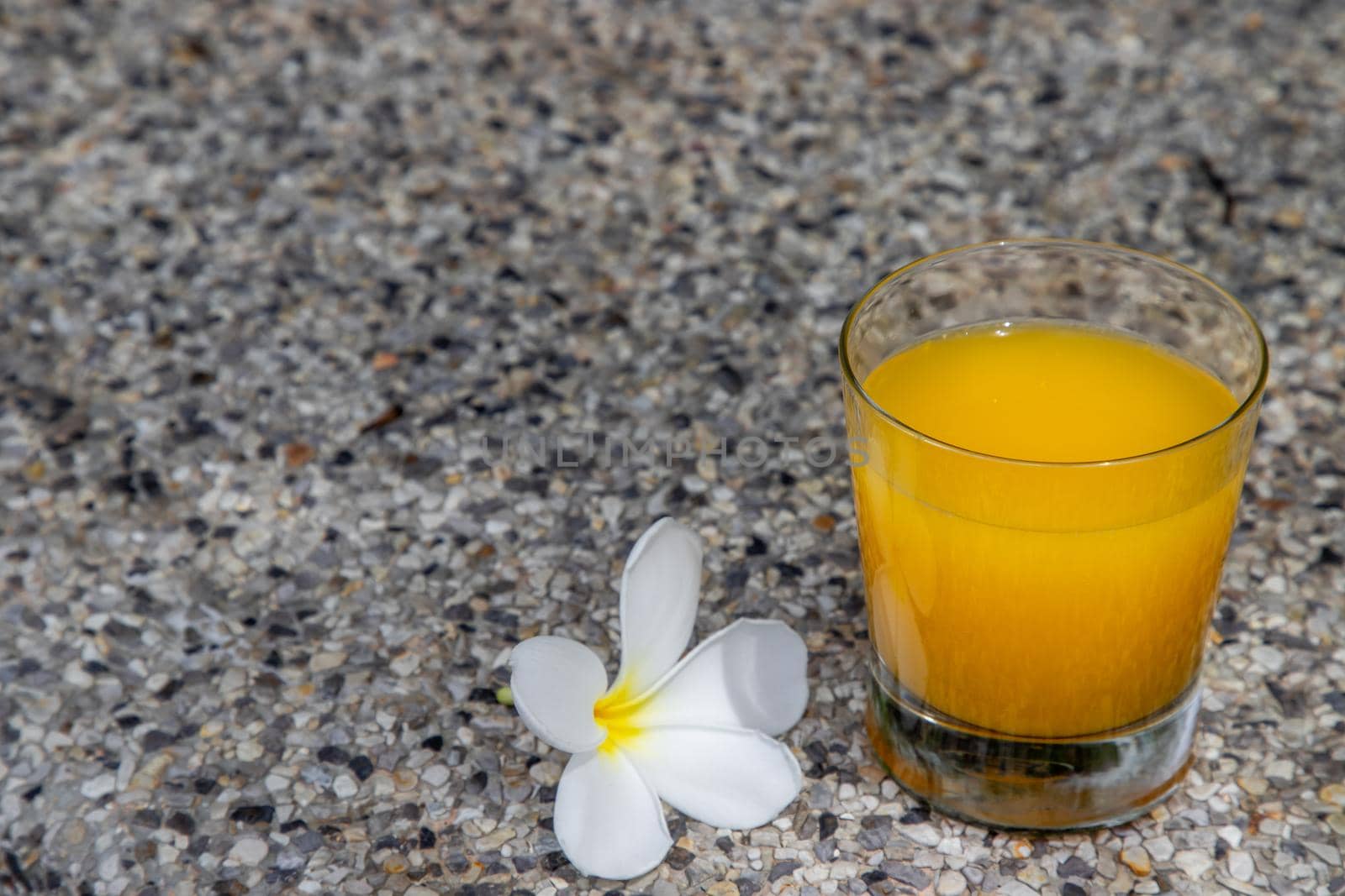 A glass of fresh orange juice with flower for a refreshment on stone background. leisure activity.