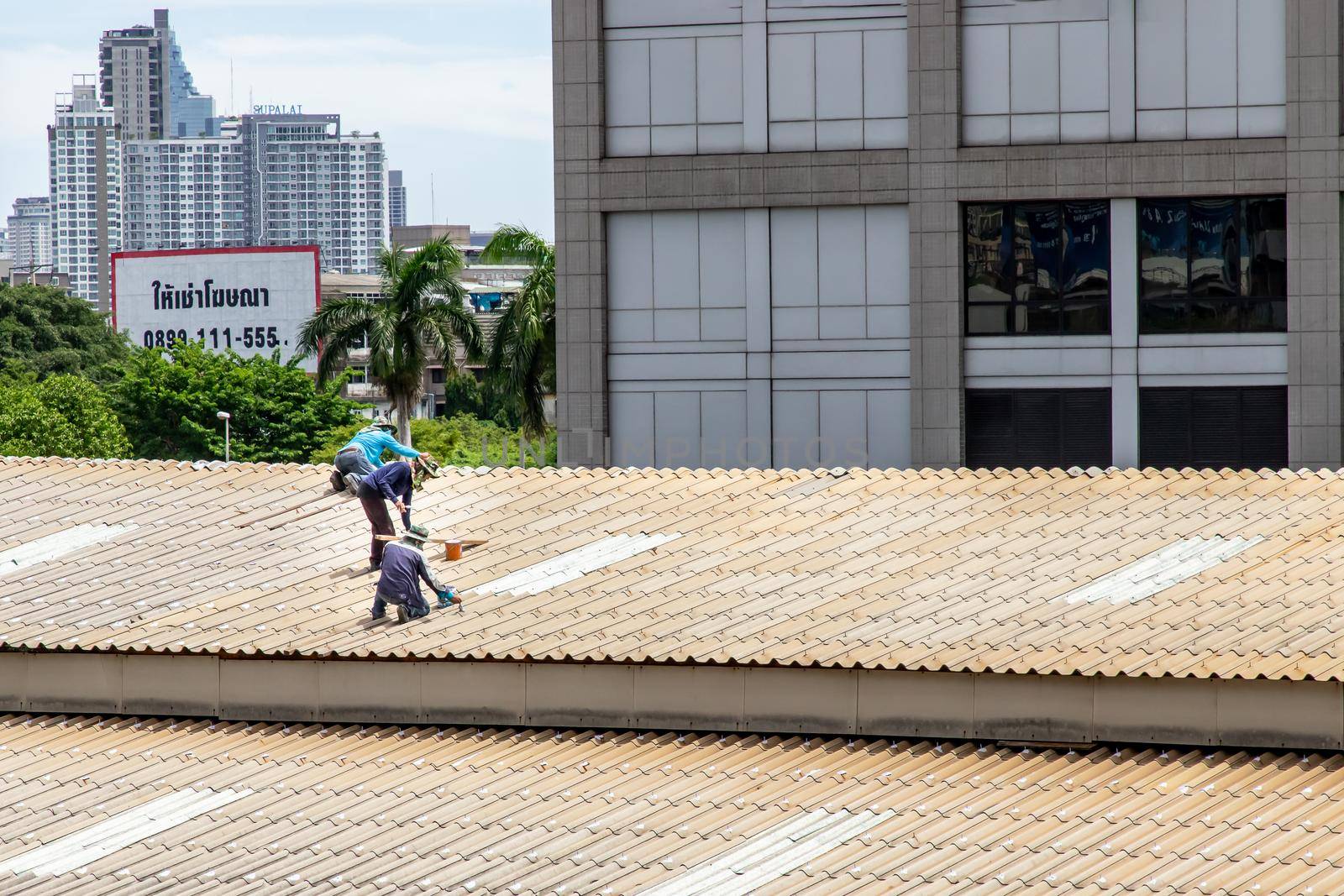 Bangkok, Thailand - 13 Jun 2020 : Two handyman workers repairing tiles on the damaged factory roof.