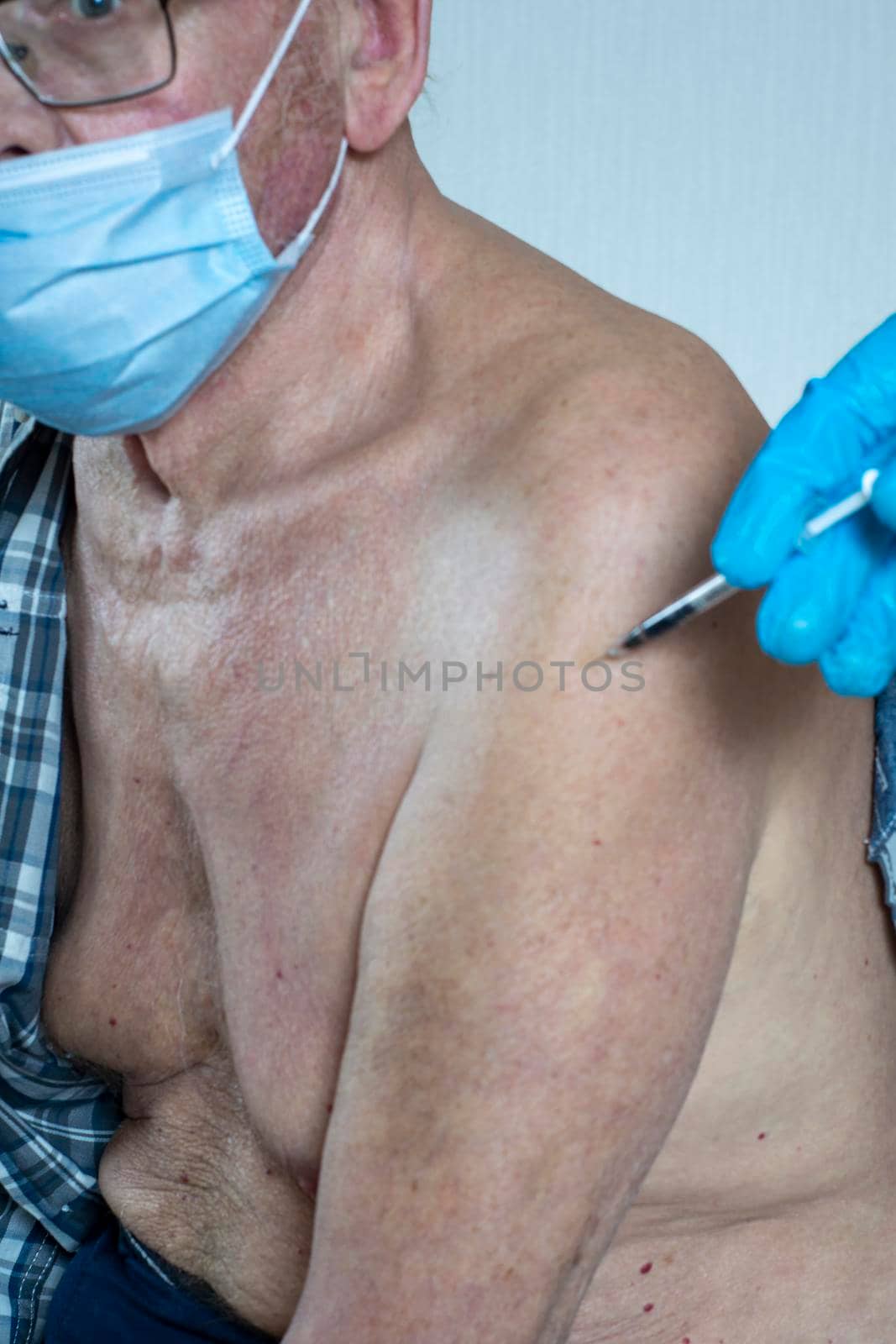 A syringe in his hand with a vaccine and a patient is an old man. Indoors in daylight. Front view. by Essffes