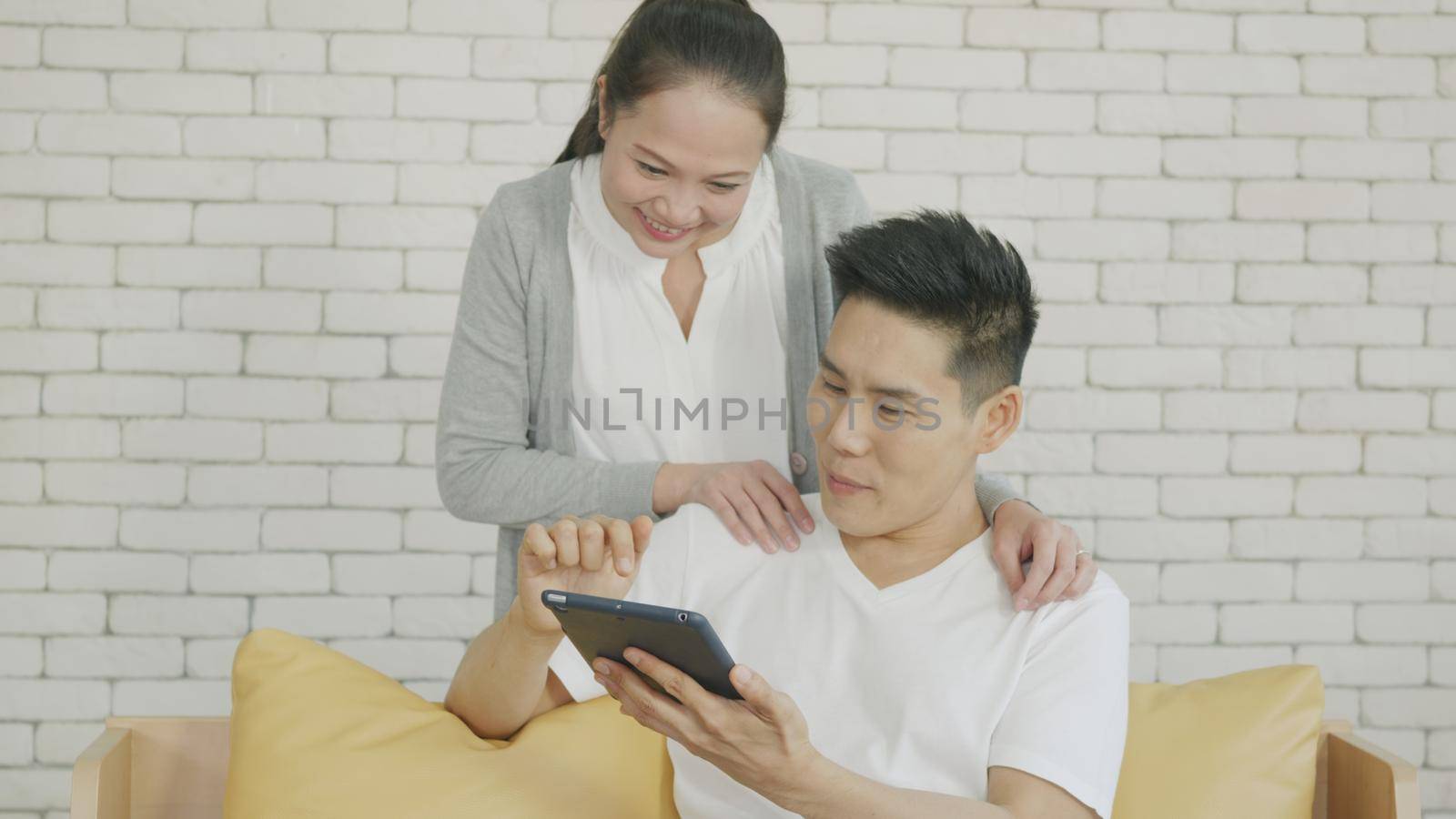 Asian family couple husband and wife work and using digital tablet. Cheerful loving couple smile shopping something online and watching social media together from home in living room,