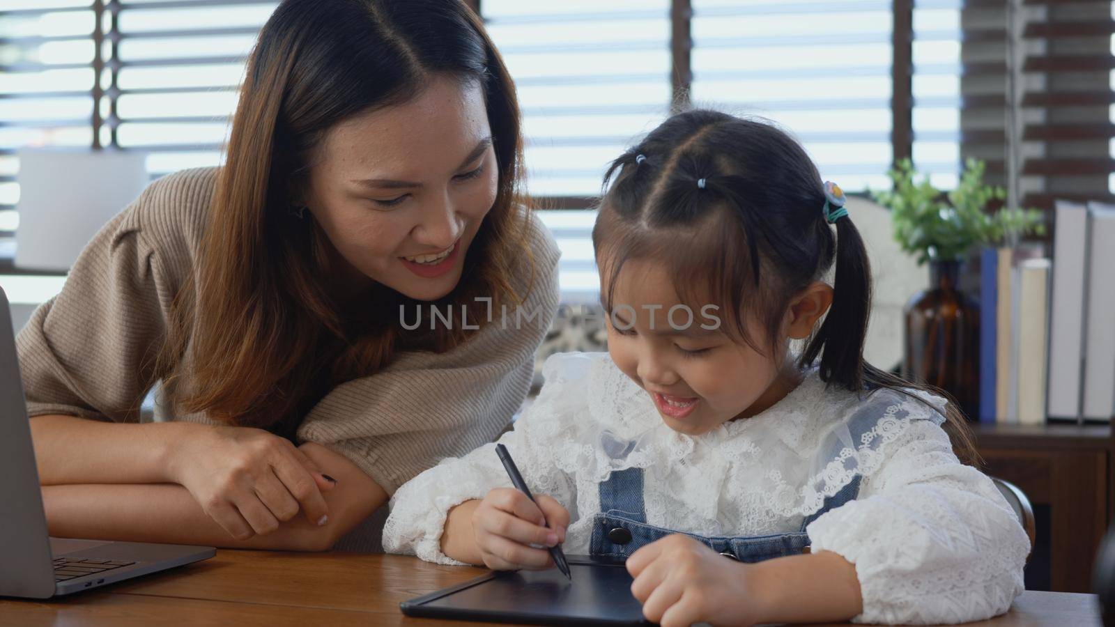 Asian young mother working with laptop computer at home and help daughter doing homework, Single mom freelancer work from home and helping his girl kid teaching homework on desk