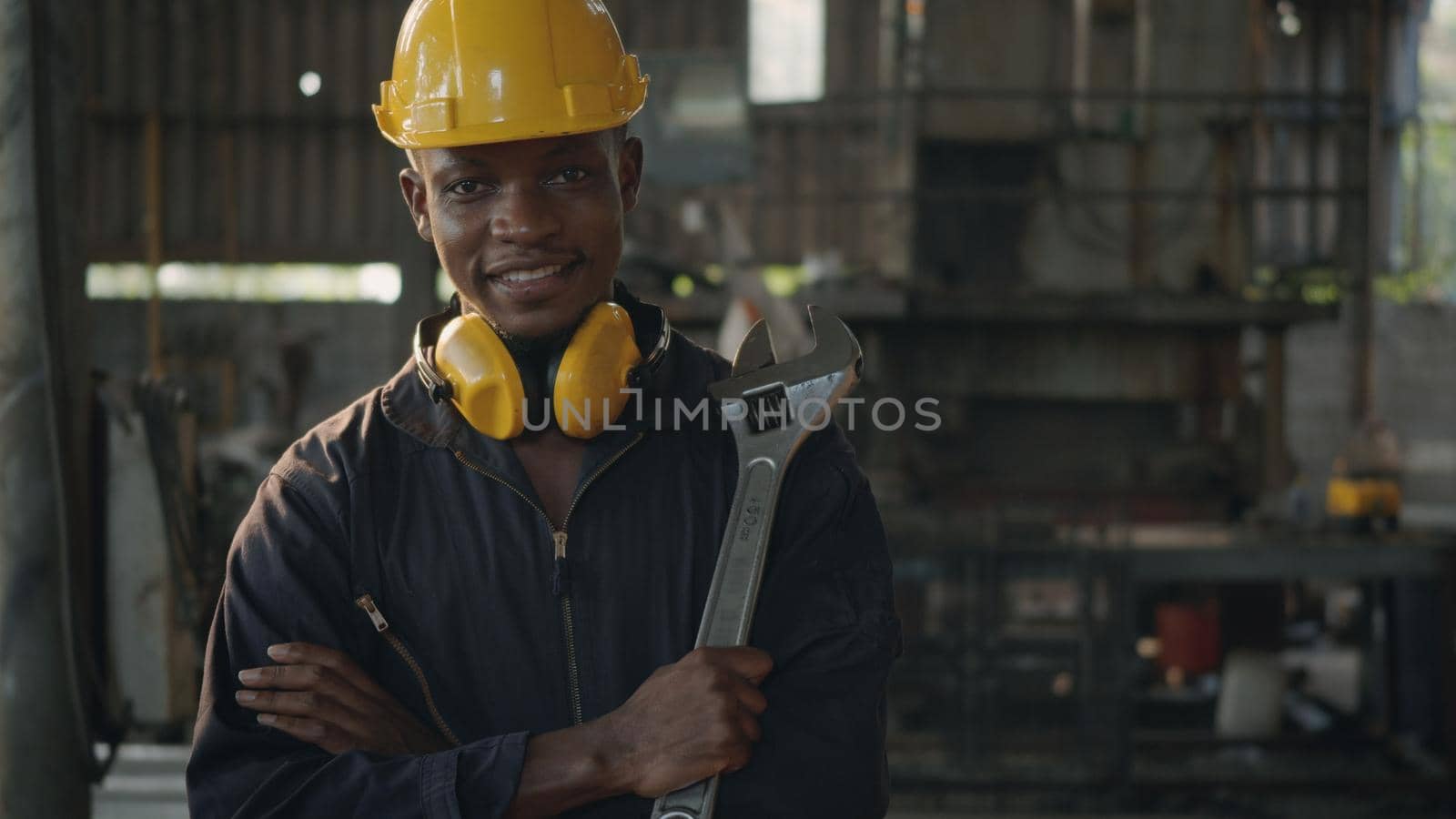 Portrait American industrial black young worker man smiling with yellow helmet in front machine, Engineer standing holding wrench tools and arms crossed at work in the industry factory.