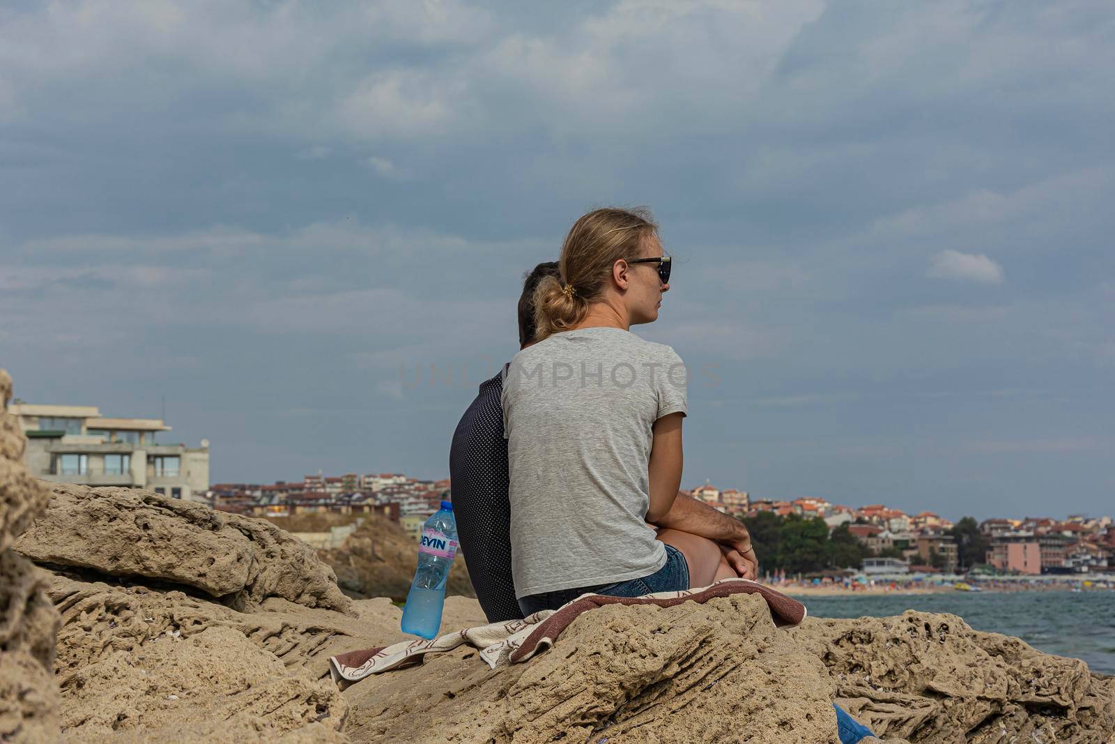 Bulgaria, Sozopol - 2018, 06 September: A girl with a guy sitting on the rocks near the sea, blurred background. by Grommik