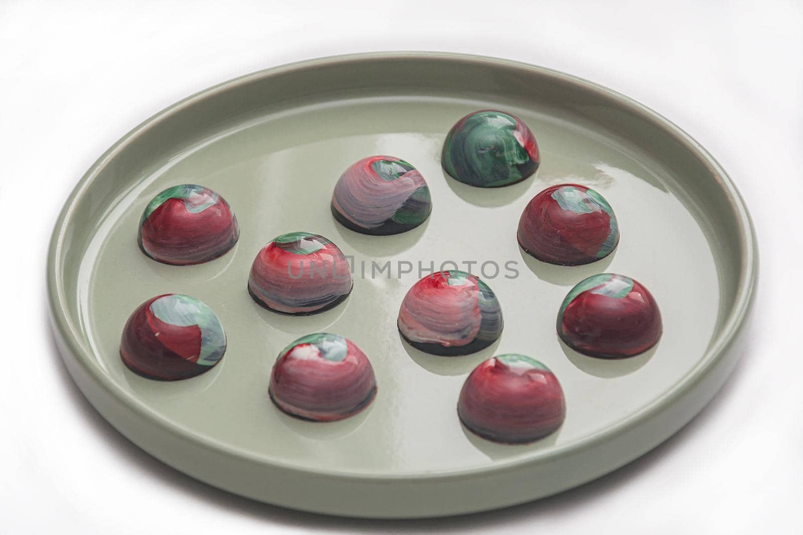 Collectible handmade tempered chocolate sweets with a glossy painted body on a round plate with blur elements by Grommik