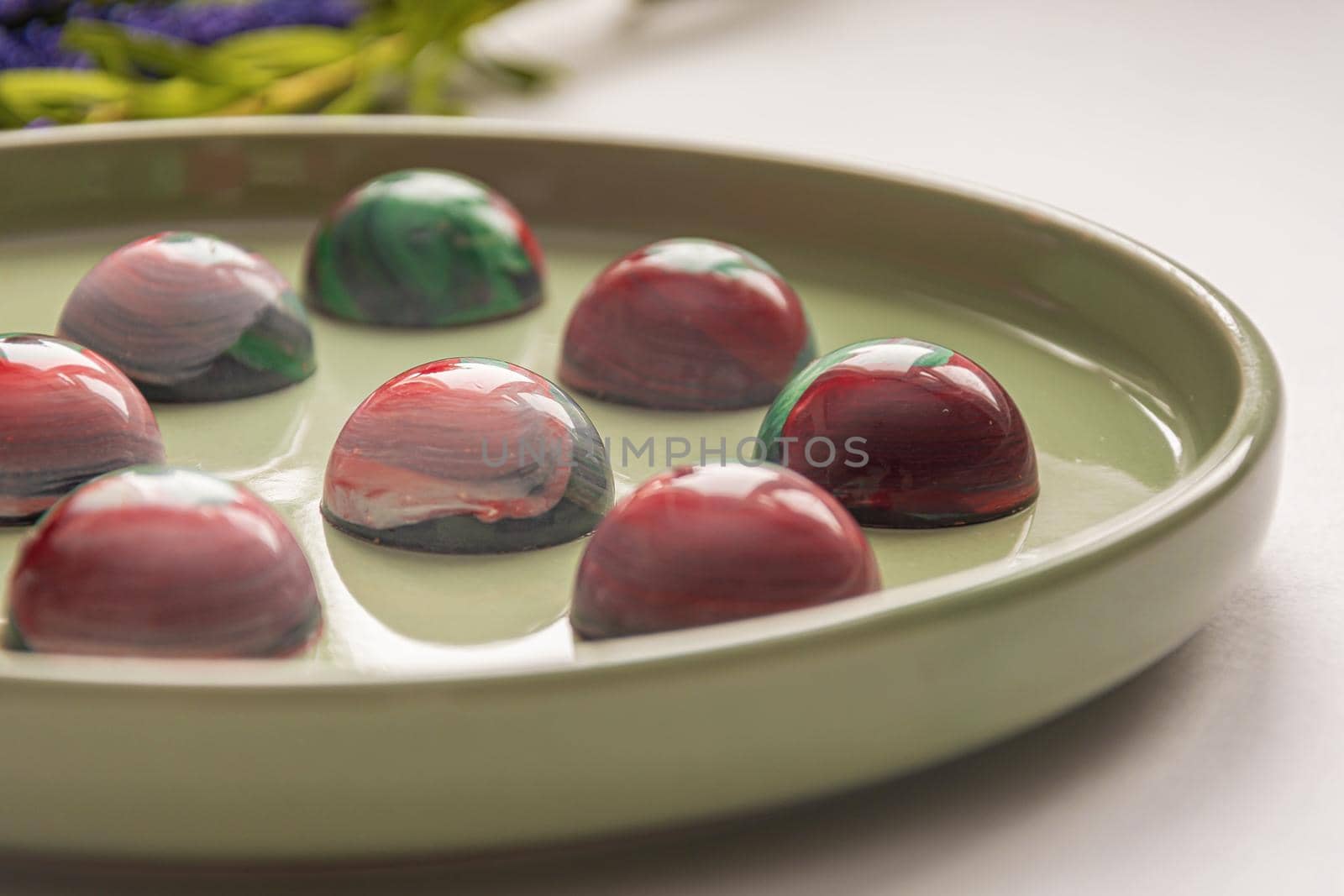 Collectible handmade tempered chocolate candies with a glossy painted body on a round plate with a blurred background and bokeh elements. Stock photography.