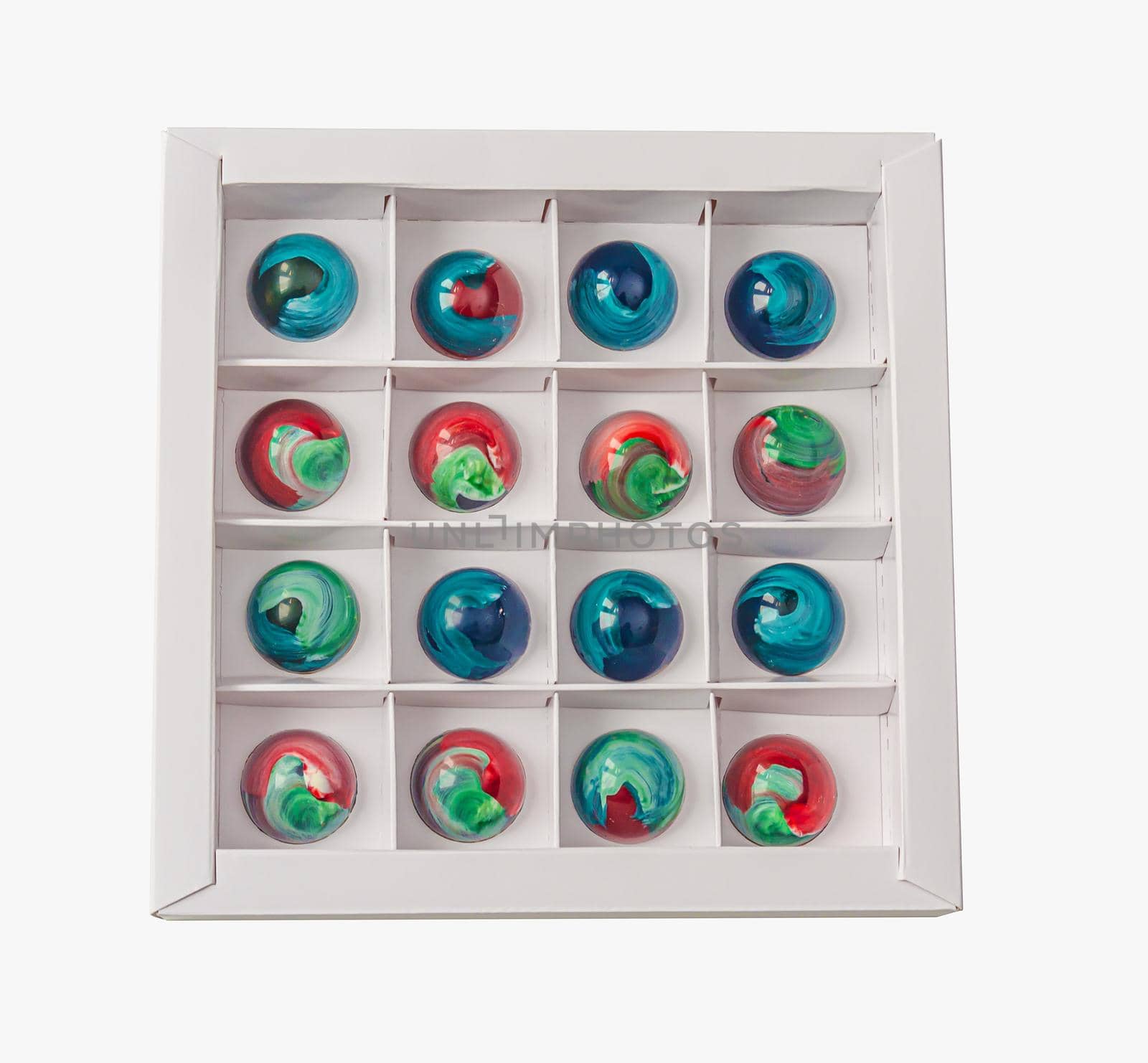 Tempered chocolate candies with glossy painted body in a box with blur elements. View from above. Stock photography.