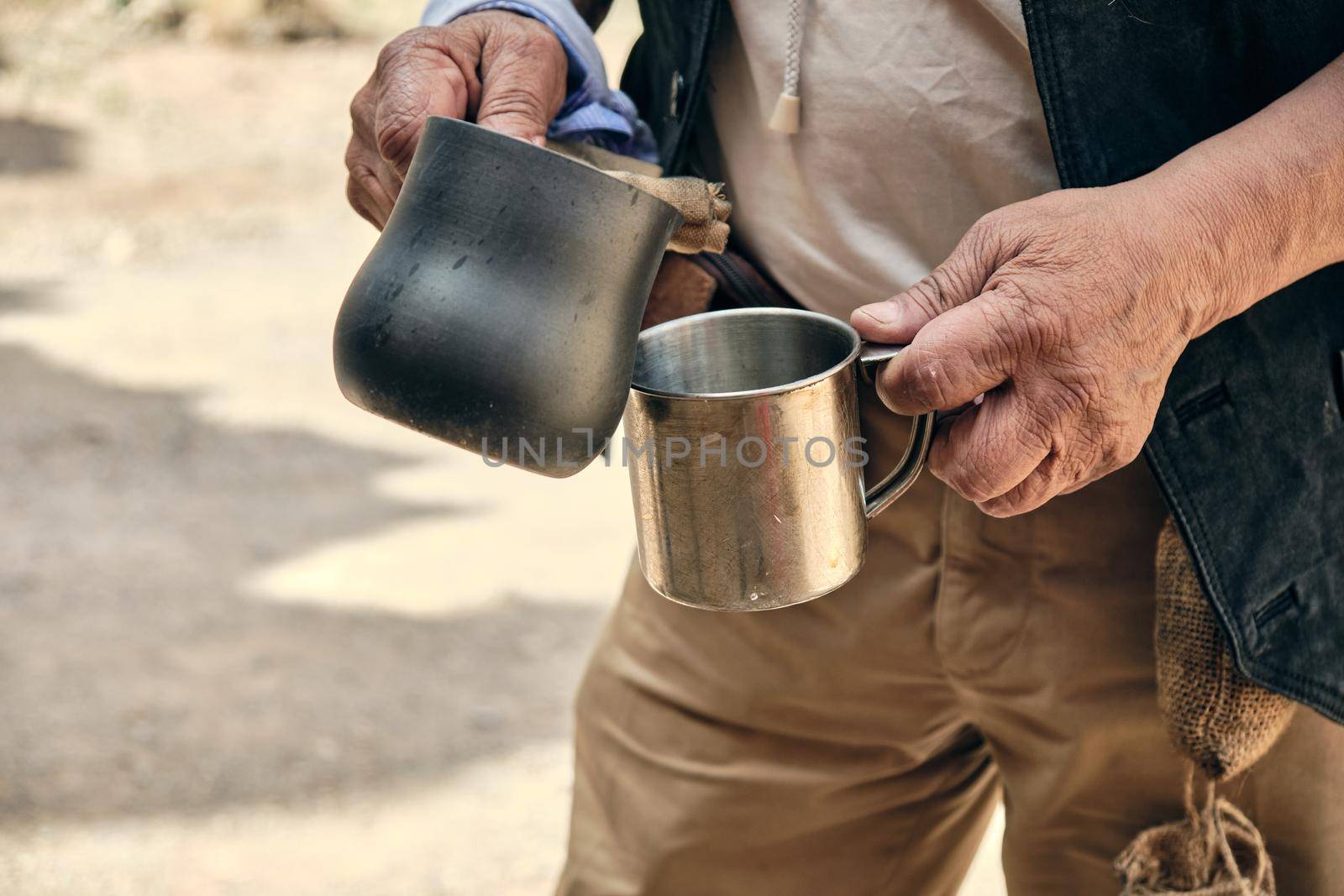 Hands of an adult man pouring hot coffee from a turk into a metal mug