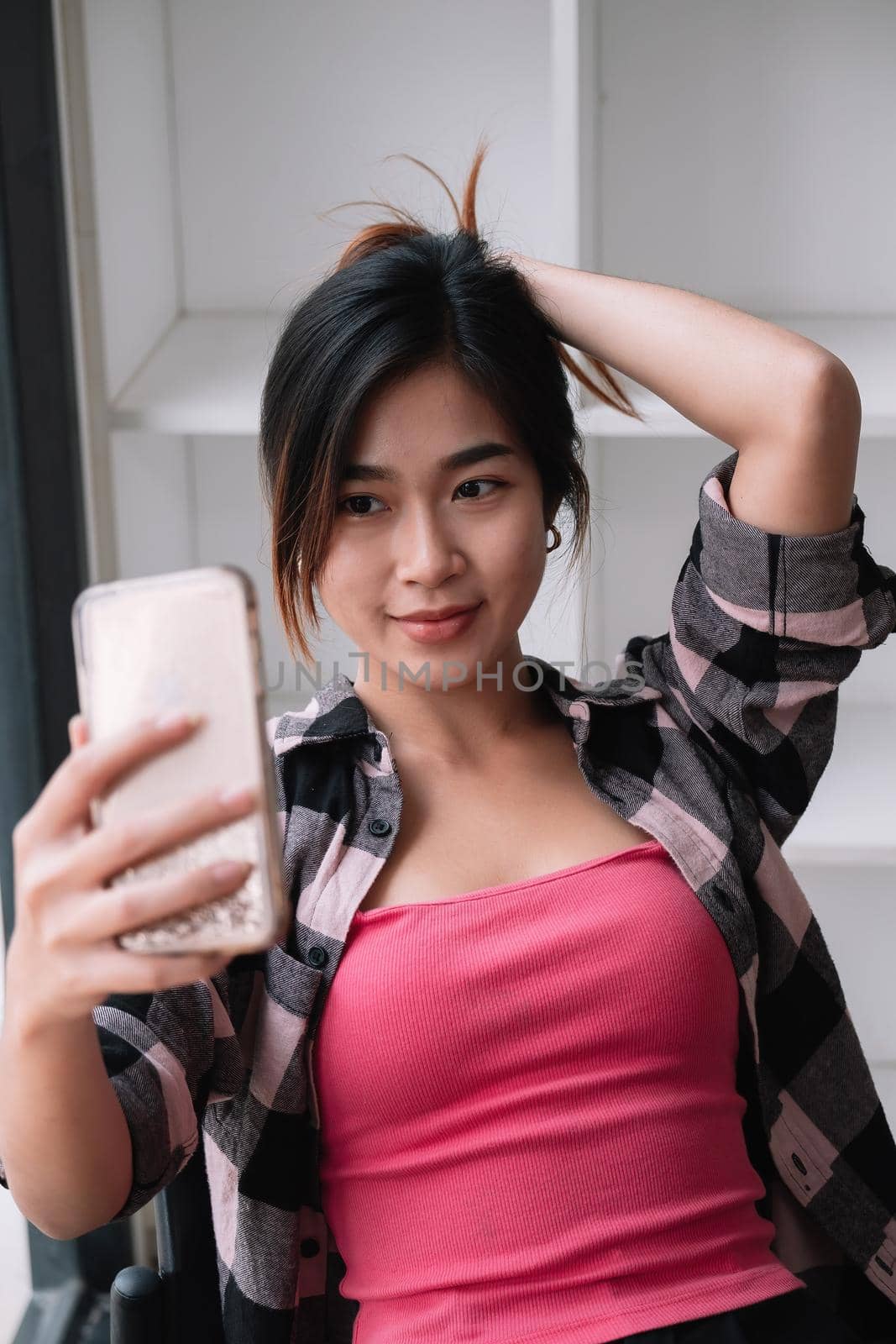 Image of young brunette asian woman smiling and taking selfie photo on cellphone at cafe shop.
