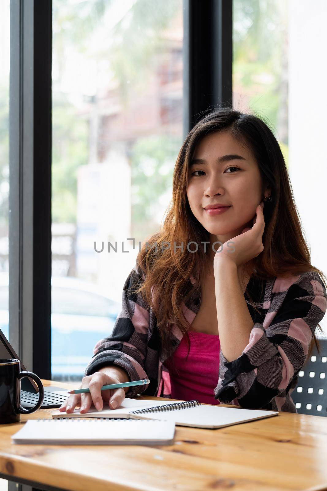 Portrait of a asian woman studying while sitting at the table with laptop computer and notebook at home
