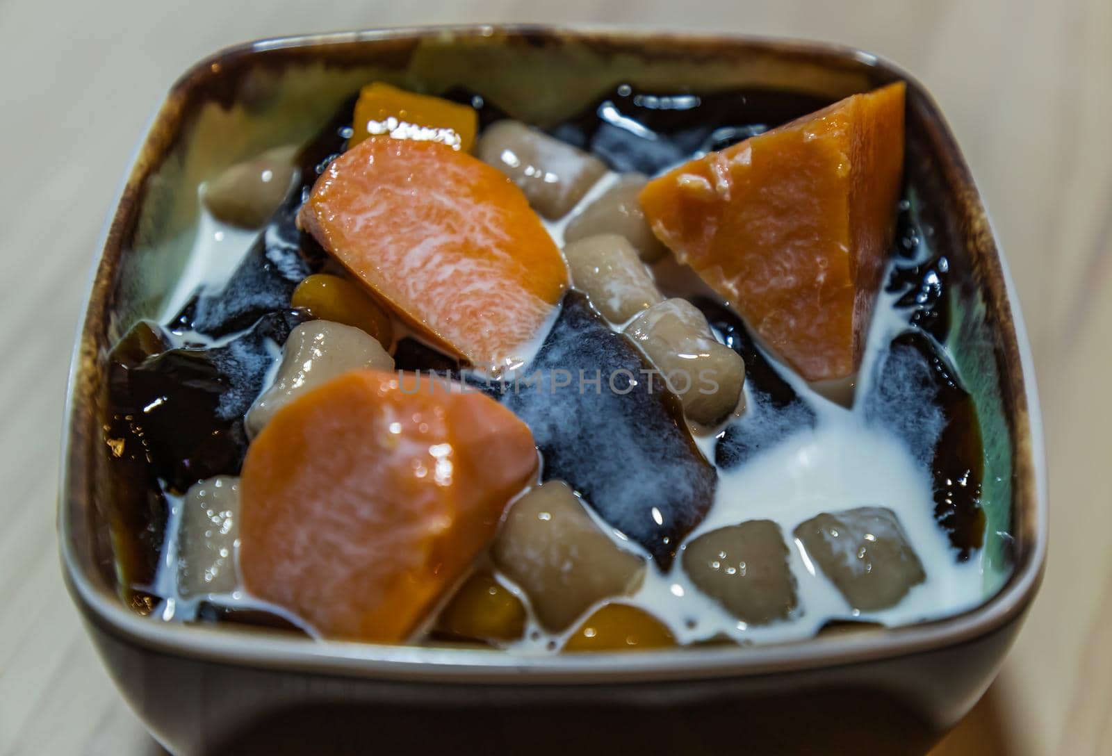 Traditional taiwanese iced dessert with Grass jelly, Taro balls, Tofu pudding, Sweet potato balls and Boba Topping with Fresh milk in Earthenware bowl. No focus, specifically.