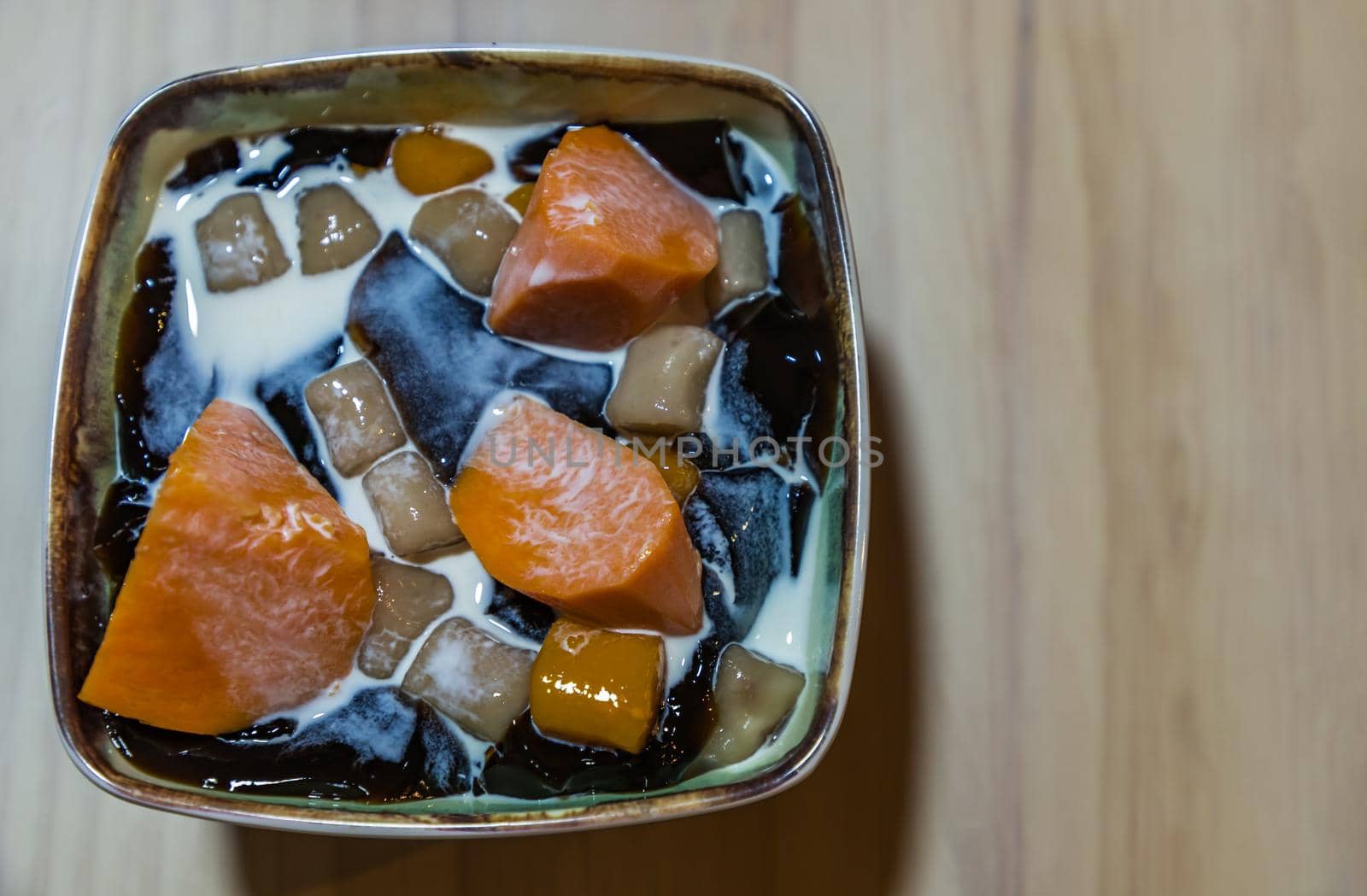 Traditional taiwanese iced dessert with Grass jelly, Taro balls, Tofu pudding, Sweet potato balls and Boba Topping with Fresh milk in Earthenware bowl. No focus, specifically.