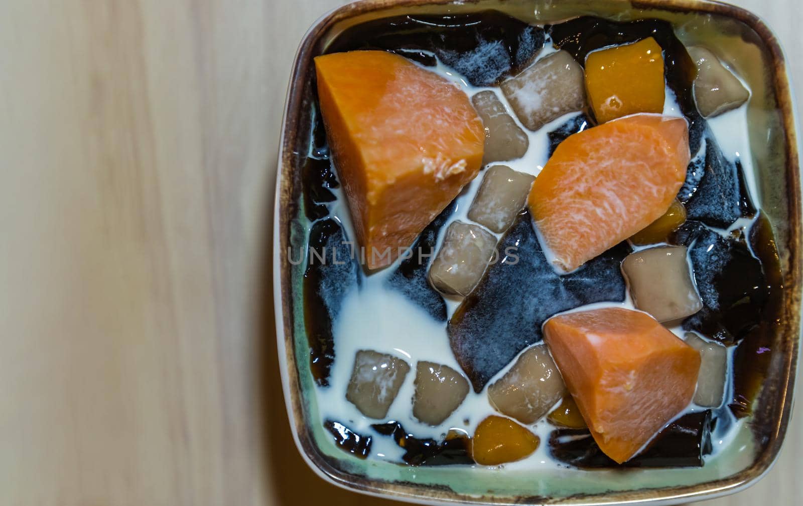 Traditional taiwanese iced dessert with Grass jelly, Taro balls, Tofu pudding, Sweet potato balls and Boba Topping with Fresh milk in Earthenware bowl. No focus, specifically.