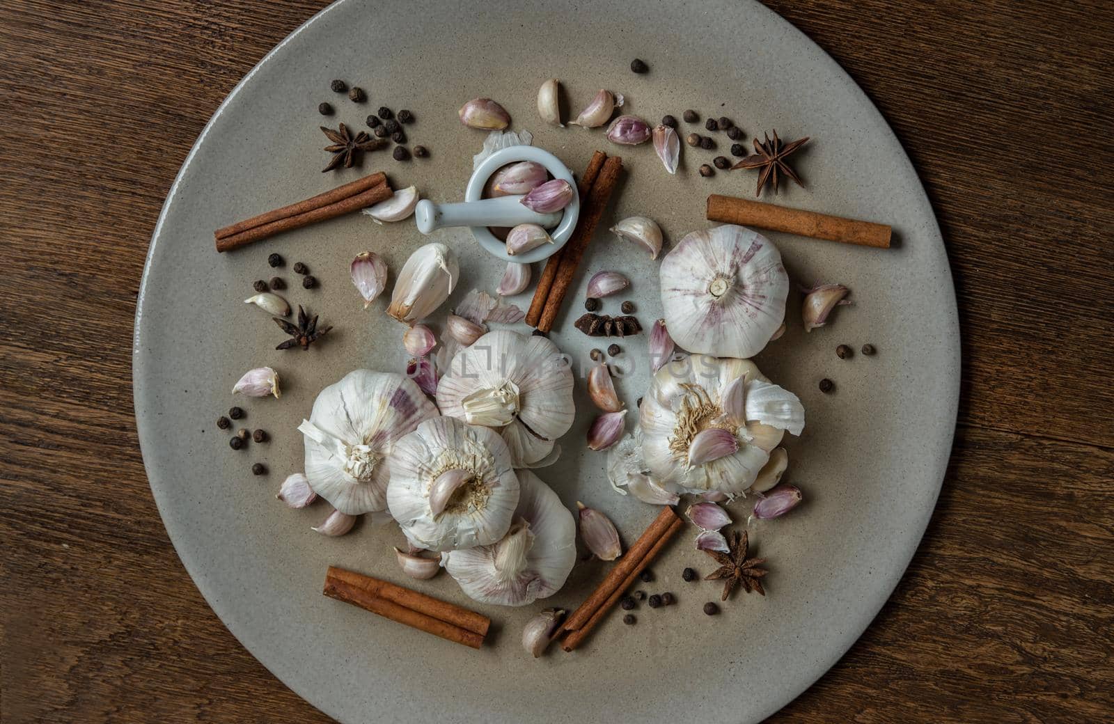 Garlic bulbs and Garlic cloves with Herbs spices, Cinnamon, Star anise and Pepper grain in Ceramic plate on Wooden rustic table. Copy space Concept of healthy food. Top view, Selective focus.