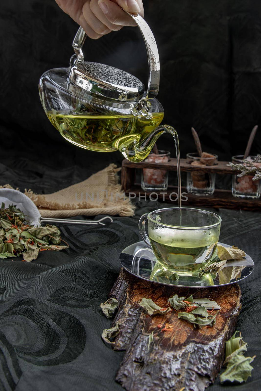 A Hot pandan leaf tea with indian marsh fleabane plant leaves and Safflower dried (Saffron substitute) is poured from the glass teapot into a glass with tea herbal and tea leave. Process brewing tea. Selective focus.