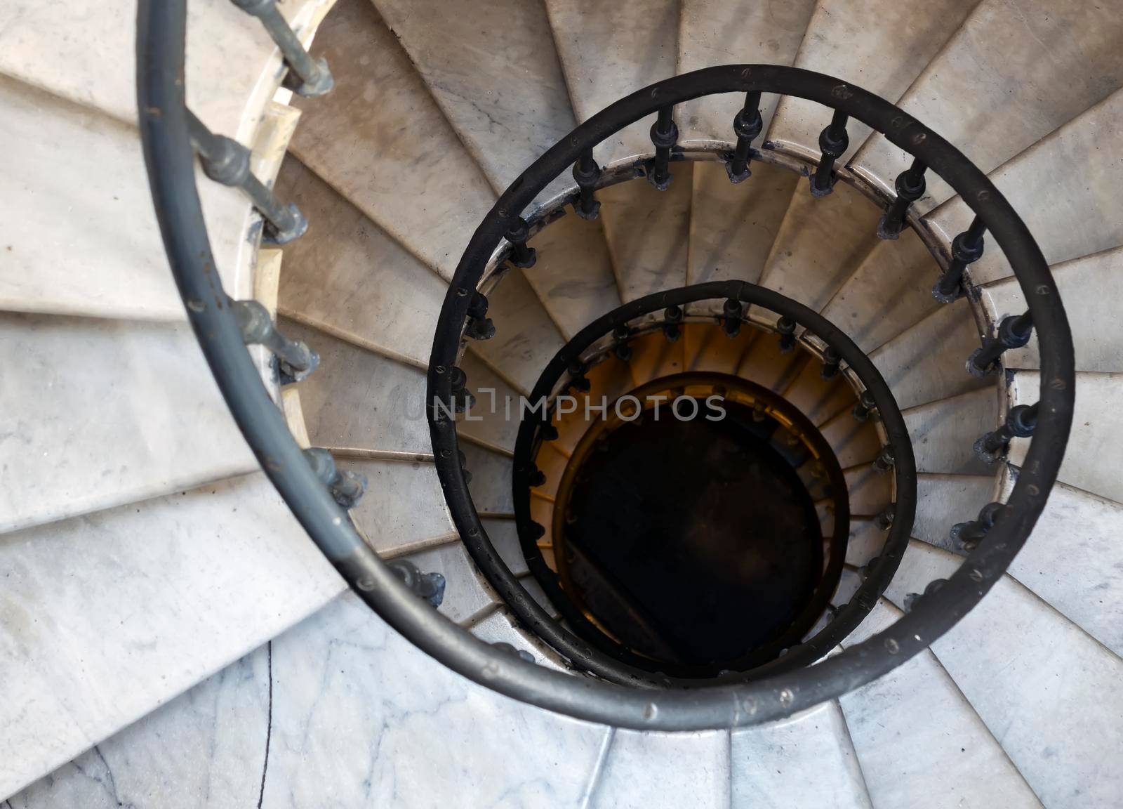 Old spiral staircase with marble steps and wrought iron handrail. Architecture and curved shapes. Top down view. Height and vertigo effect