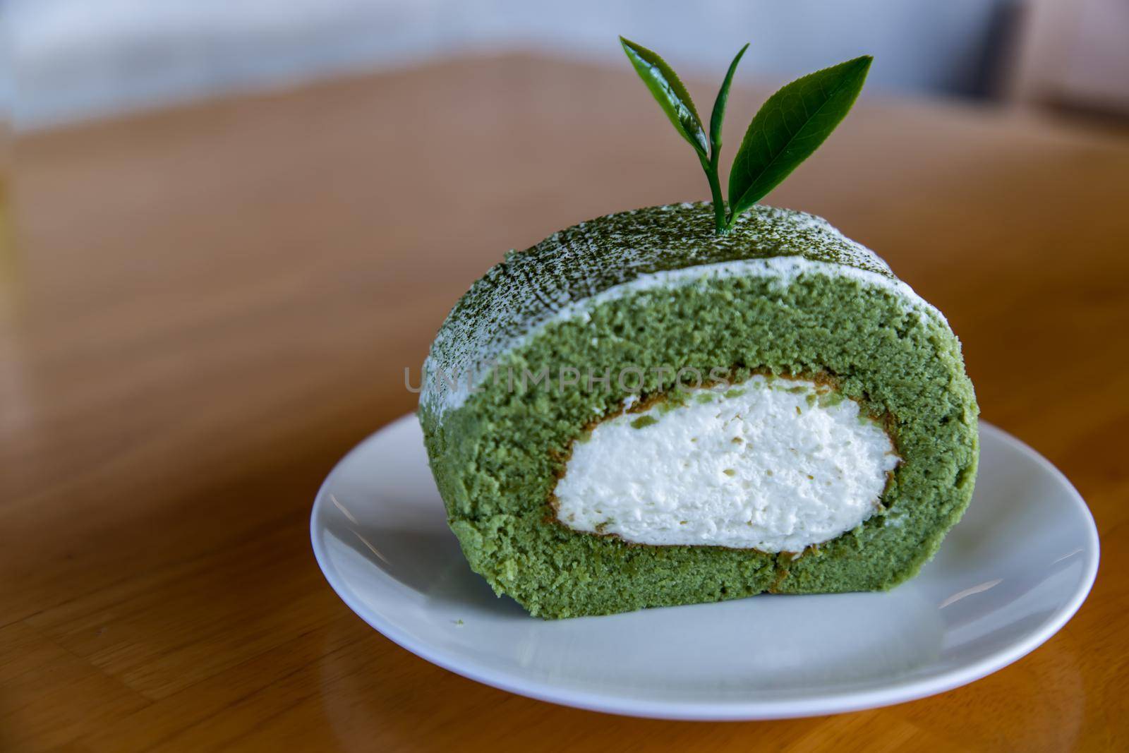 Matcha green tea roll cake and Decor with Tea leaf on White plate on wooden table. Sweet or dessert, Focus and blur.