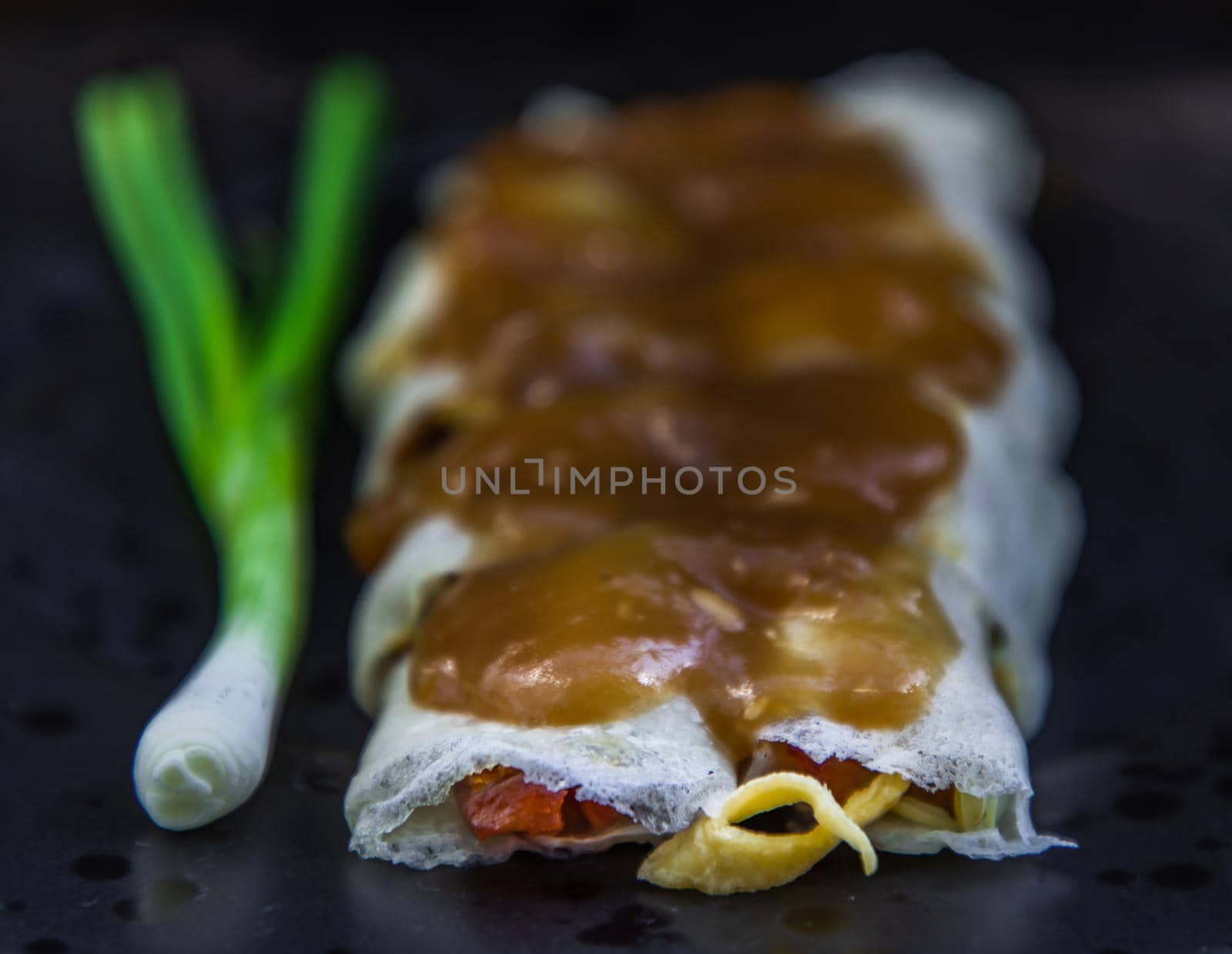 Close-up of Thai fresh spring rolls Topped with Sweet sauce with Spring onions on black plate. Selective focus.