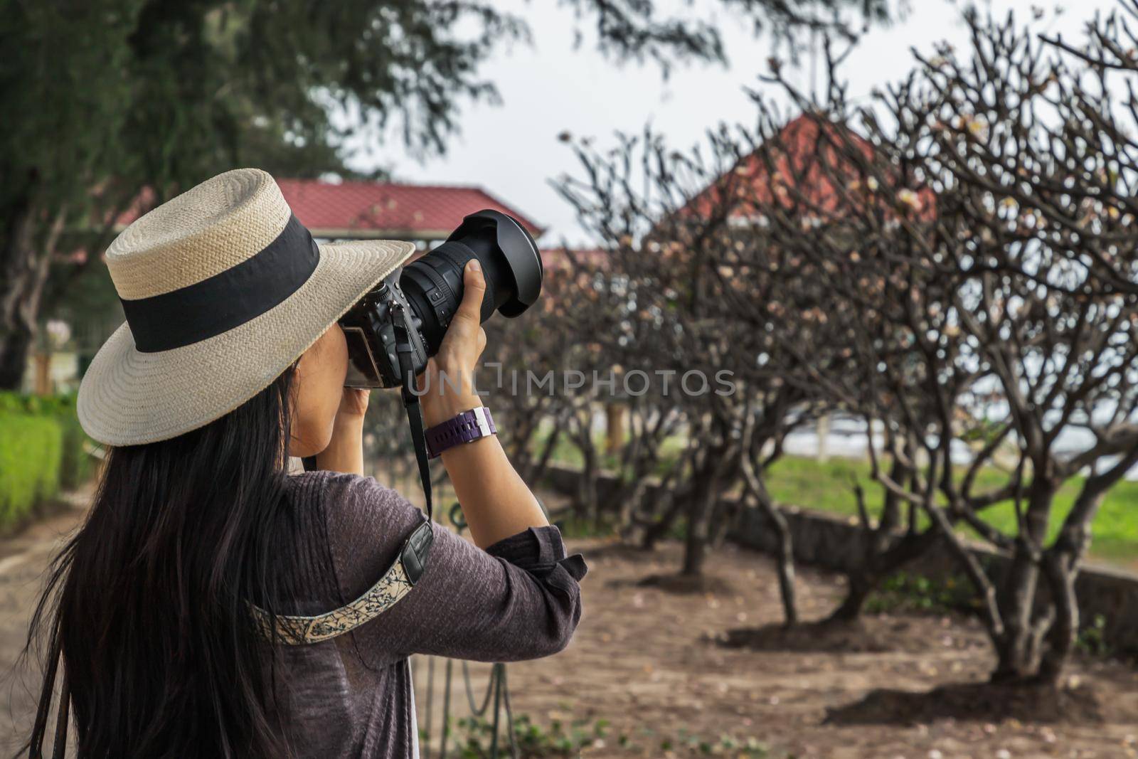 Young woman wearing a white hat and taking a camera to take pictures of the scenery on the sea beach. Traveling and photography. No focus, specifically.