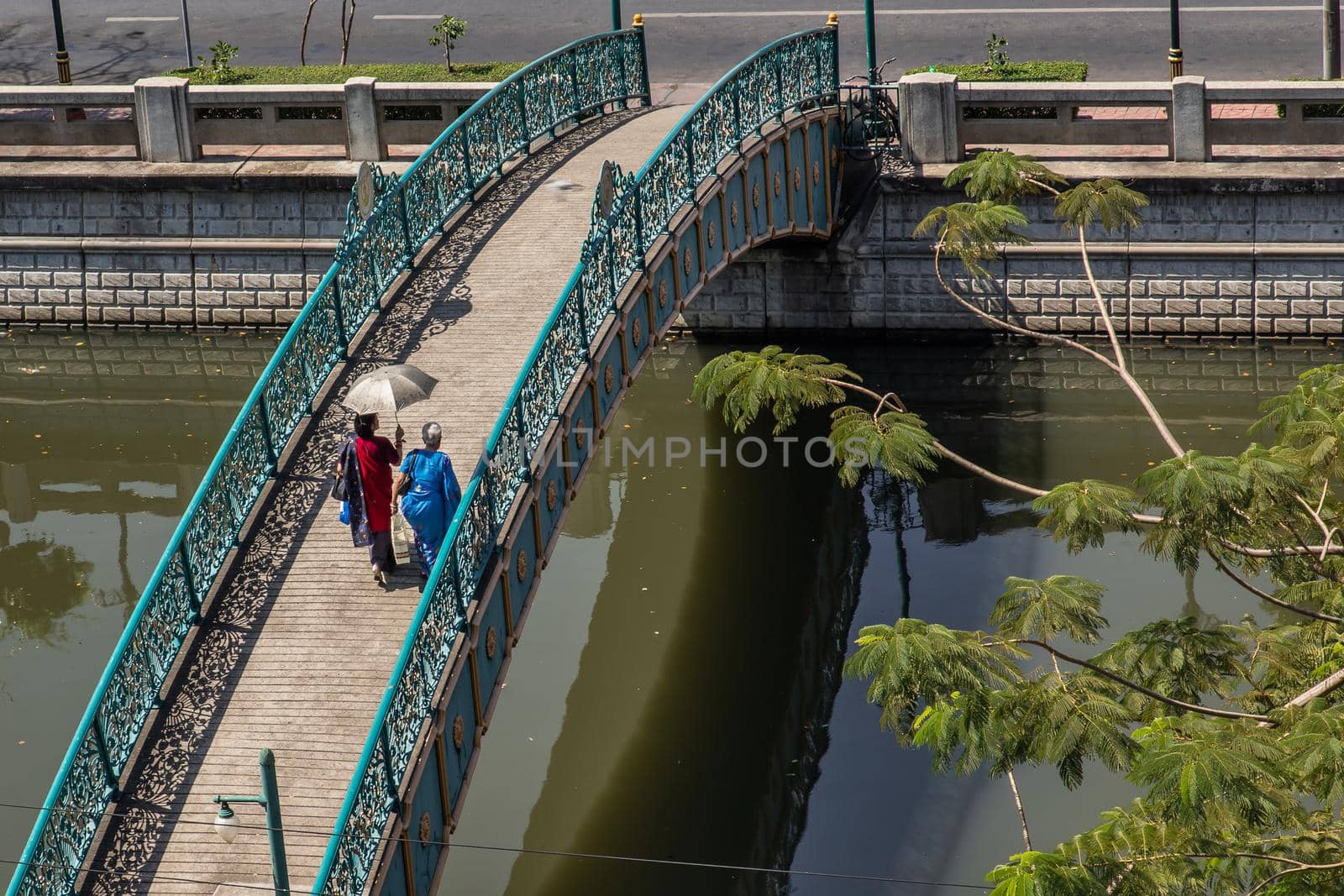 Two indian woman in traditional attire walking on a bridge over a small canal. Selective focus.