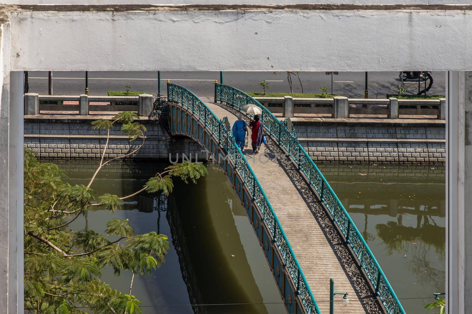Two indian woman in traditional attire walking on a bridge over a small canal. looks through the window frames in abandoned building. Selective focus.